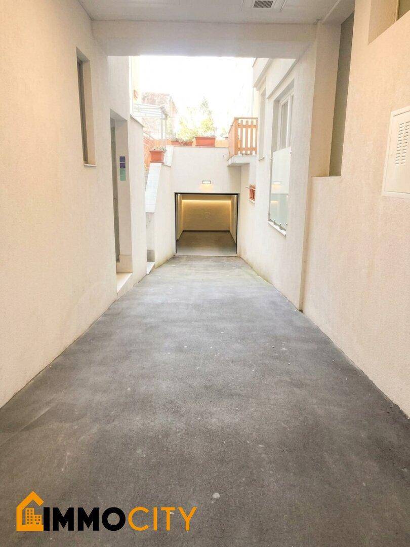 Zufahrt zu einer Tiefgarage, umgeben von hellen Gebäudewänden und mit Blick auf den Himmel.
