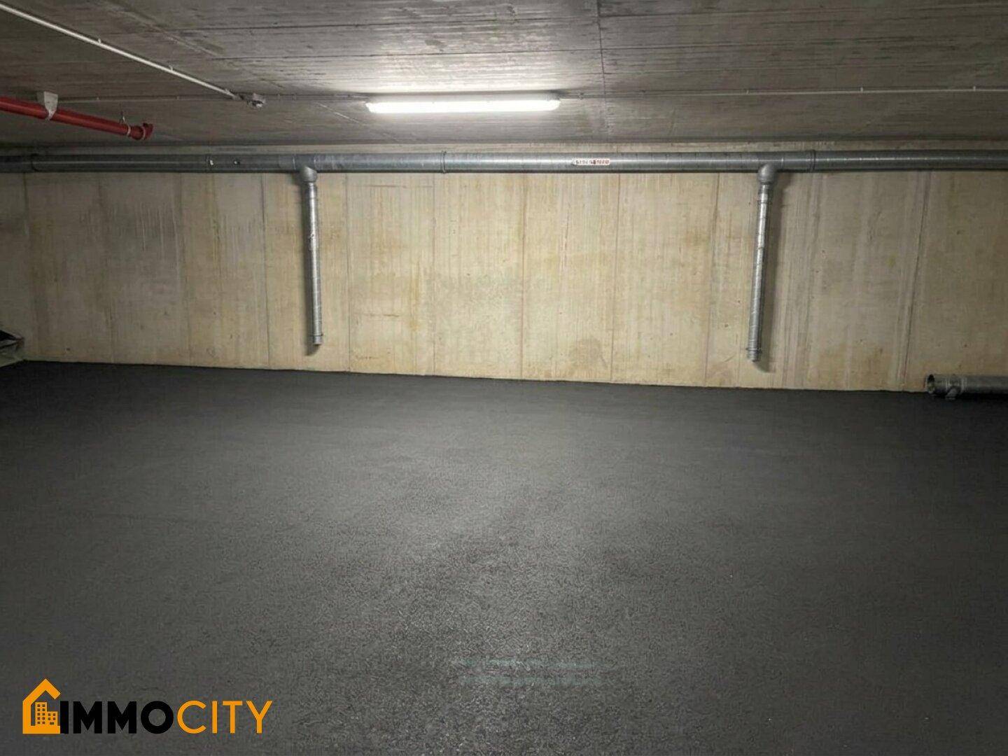 Leerer Raum in einer Tiefgarage mit Betonwänden und -decke sowie horizontalen Rohren an der Wand.