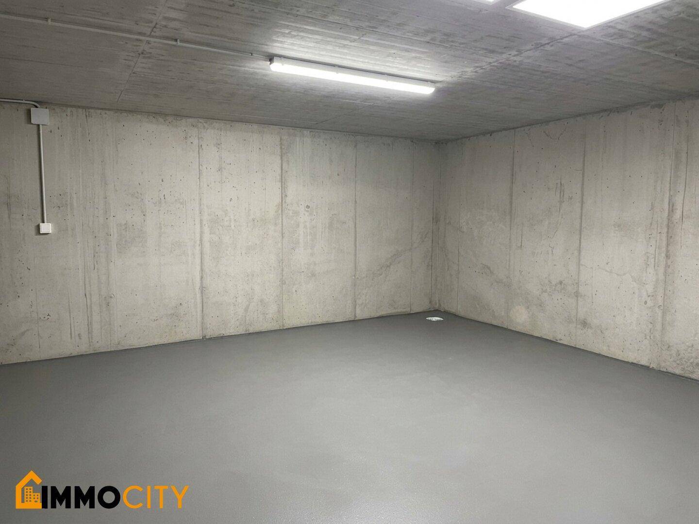 Heller, leerer Raum in einer Tiefgarage mit glattem Betonboden und Wänden unter künstlicher Beleuchtung.