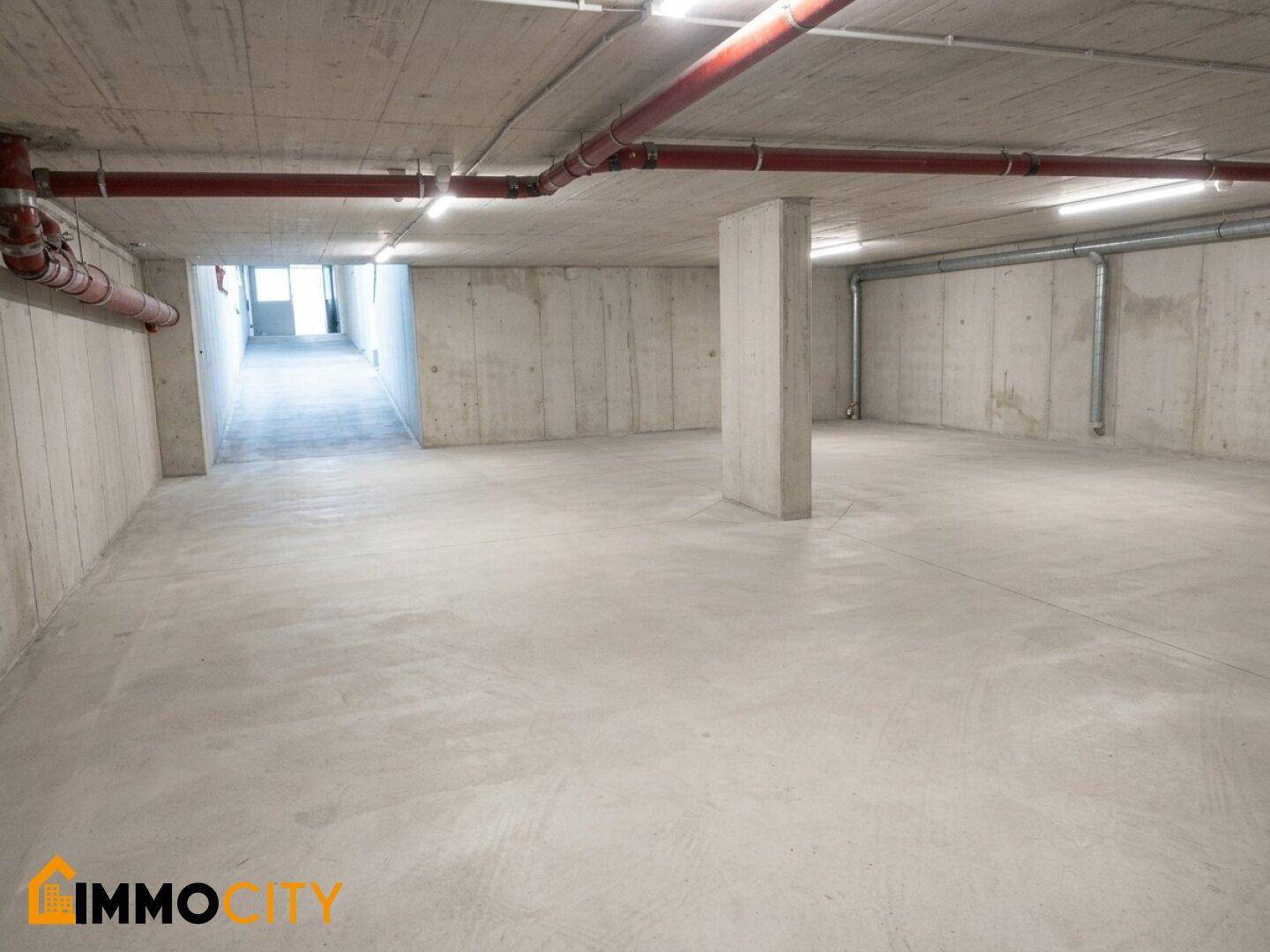 Geräumige Tiefgarage mit Betonwänden und -boden sowie sichtbaren roten Rohrleitungen an der Decke.