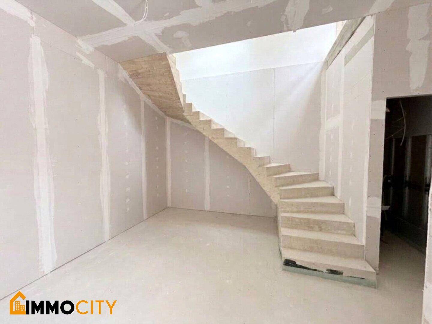Unfertiger Innenraum mit einer freitragenden Treppe und Trockenbauwänden, bereit für den weiteren Ausbau.