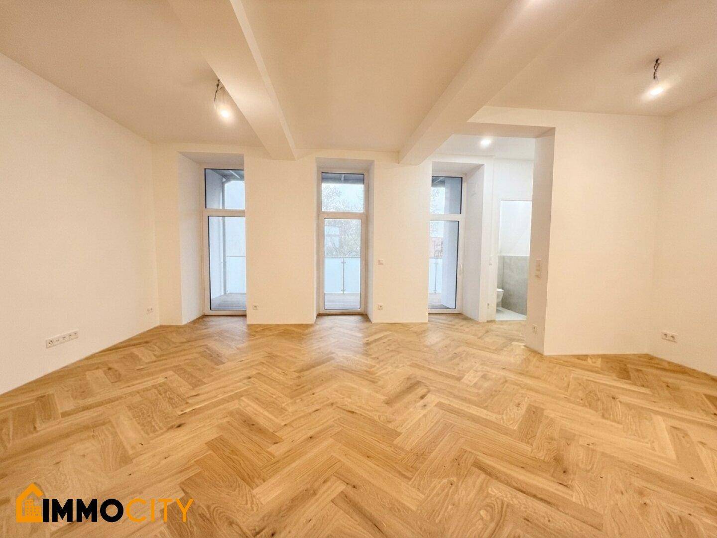 Heller Wohnraum mit elegantem Fischgrätparkett und mehreren Fenstern, die viel Licht hereinlassen.