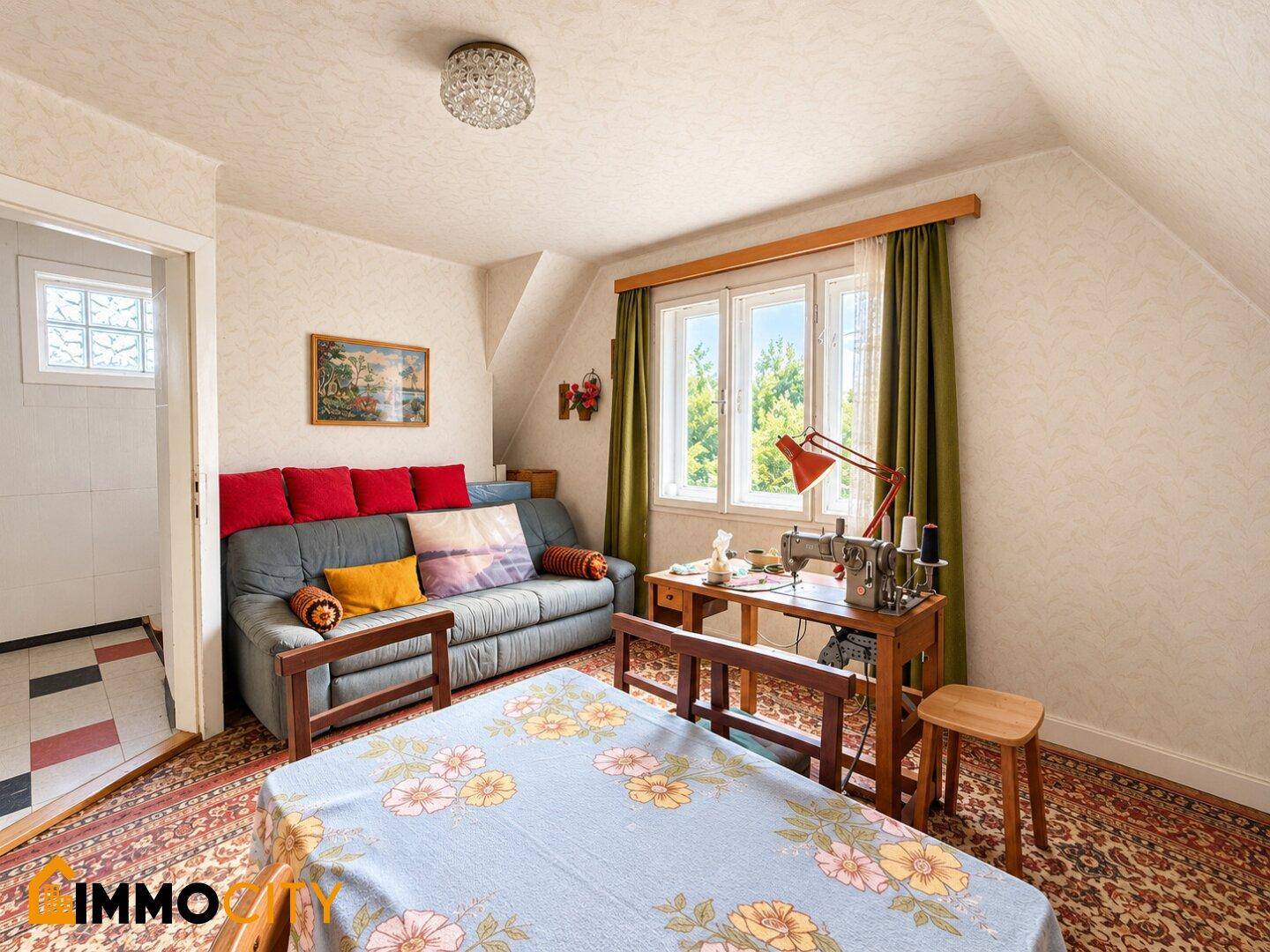 Gemütliches Dachzimmer mit Sofa, Nähmaschine und Blick ins Grüne.