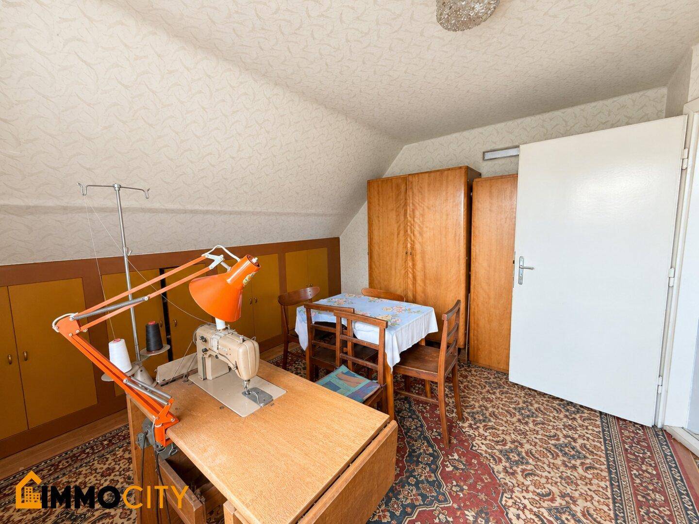 Dachzimmer mit Nähmaschine, Holzkleiderschränken und Stauraum unter der Schräge.