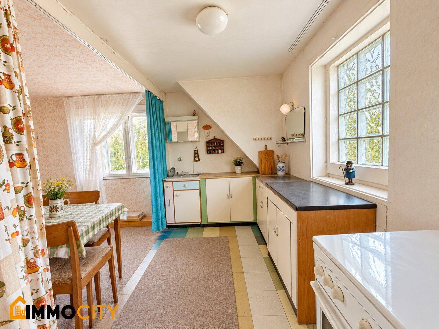 Rustikale Küche mit Essbereich, Dachschräge und Blick ins Grüne durch Fenster.