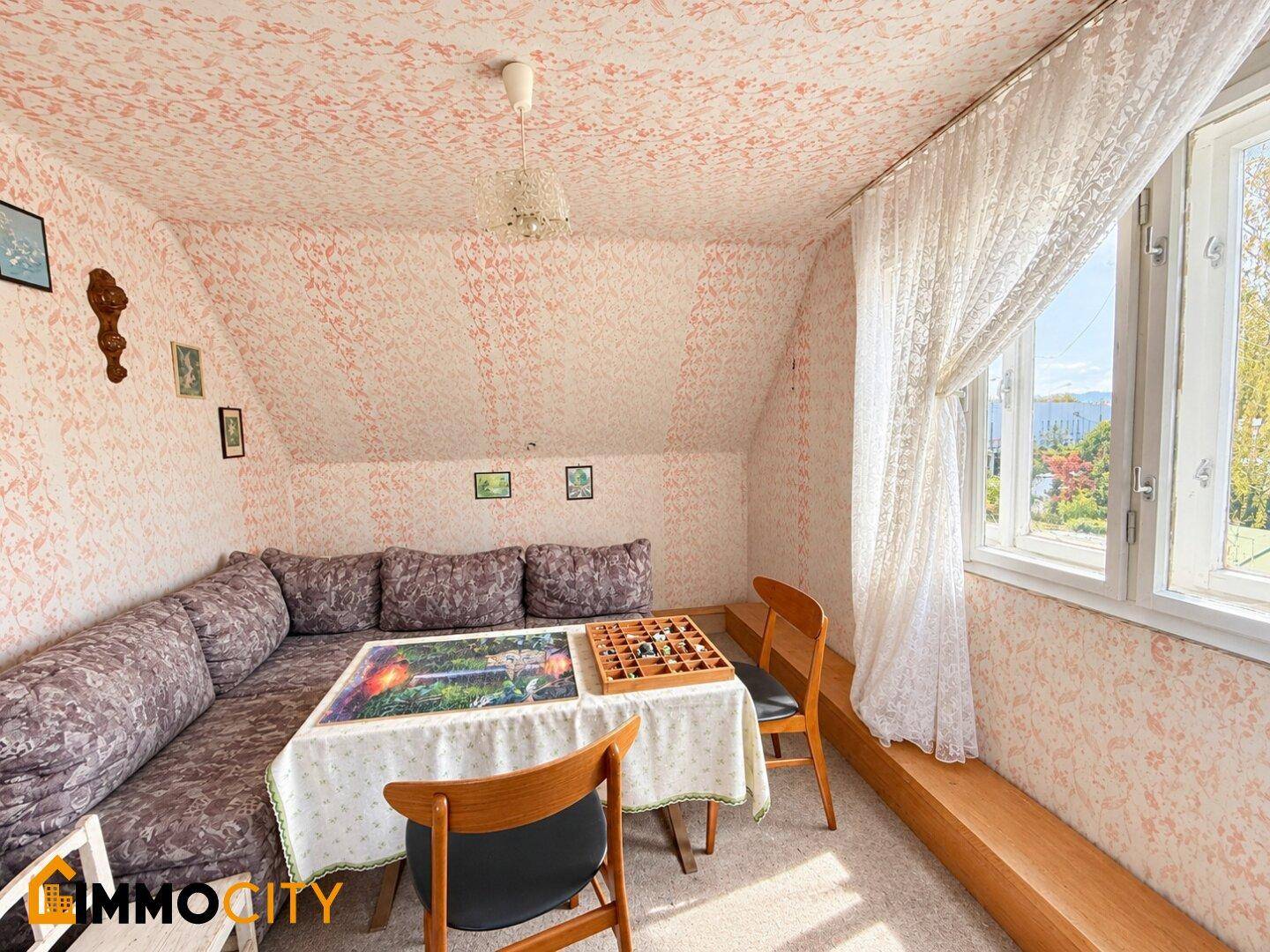 Helles Dachzimmer mit Ecksofa, Tisch und Fenster mit Blick ins Freie.