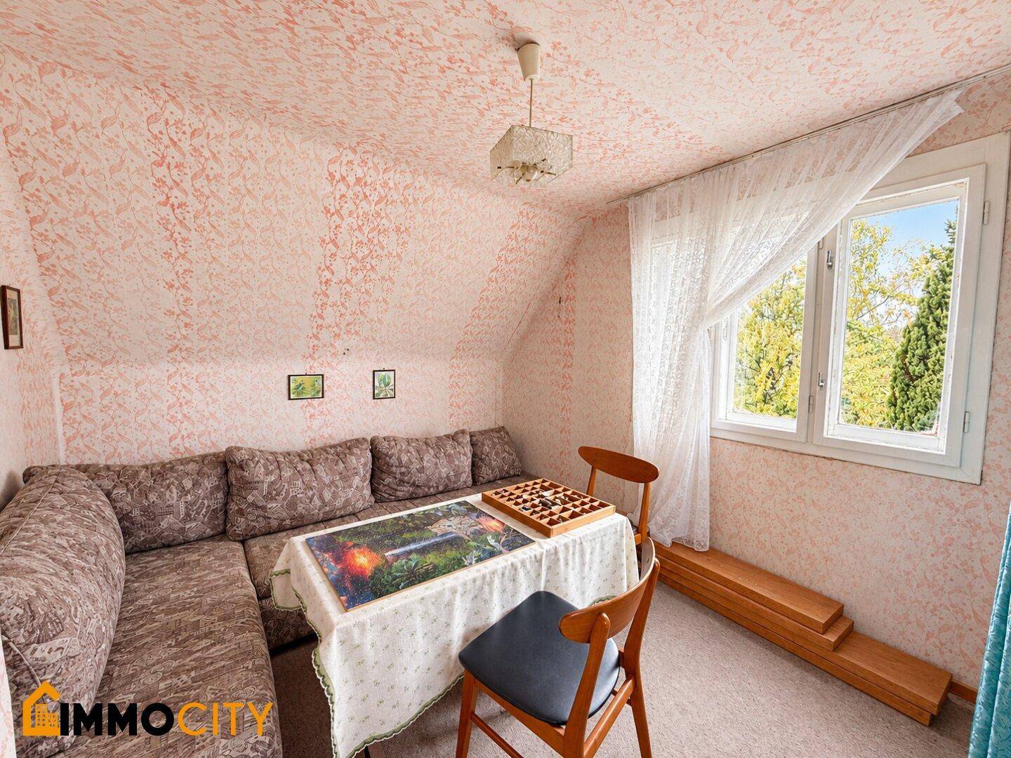 Gemütliches Dachzimmer mit Ecksofa, Tisch und Blick aus dem Fenster.