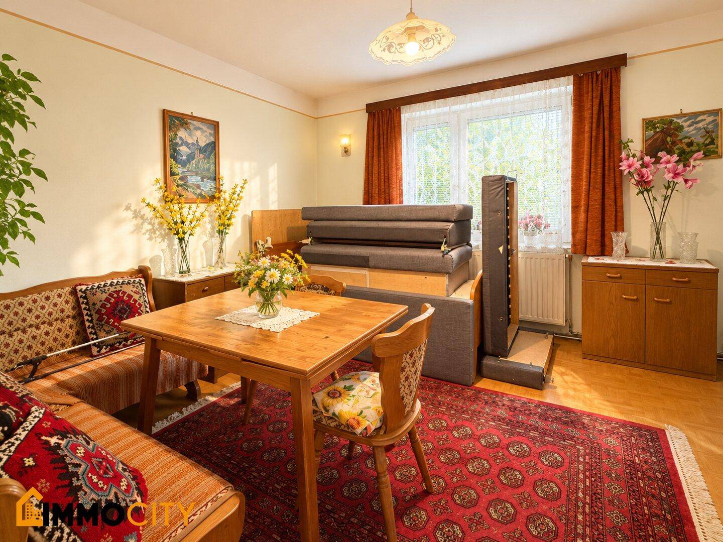 Gemütlicher Wohn-Essbereich mit Holztisch, traditionellem Teppich und Schlafsofa.