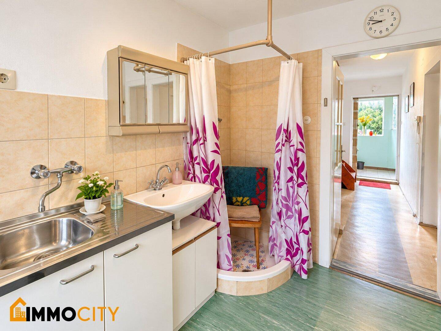 Kleines Badezimmer mit Dusche, Waschbecken und integrierter Küchenzeile.