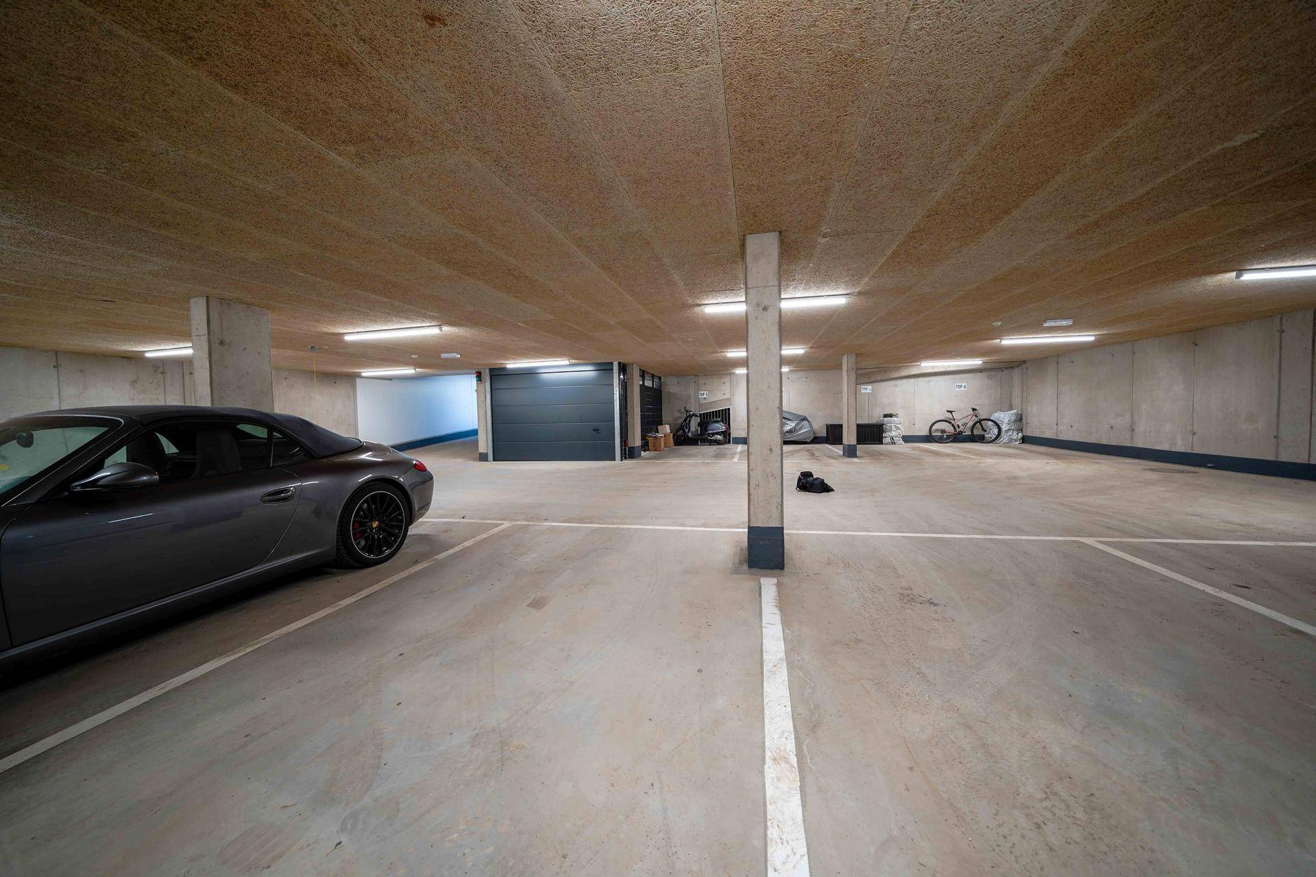 Weitläufige Tiefgarage mit mehreren Stellplätzen, Betonpfeilern und einem Lagerraum im Hintergrund.