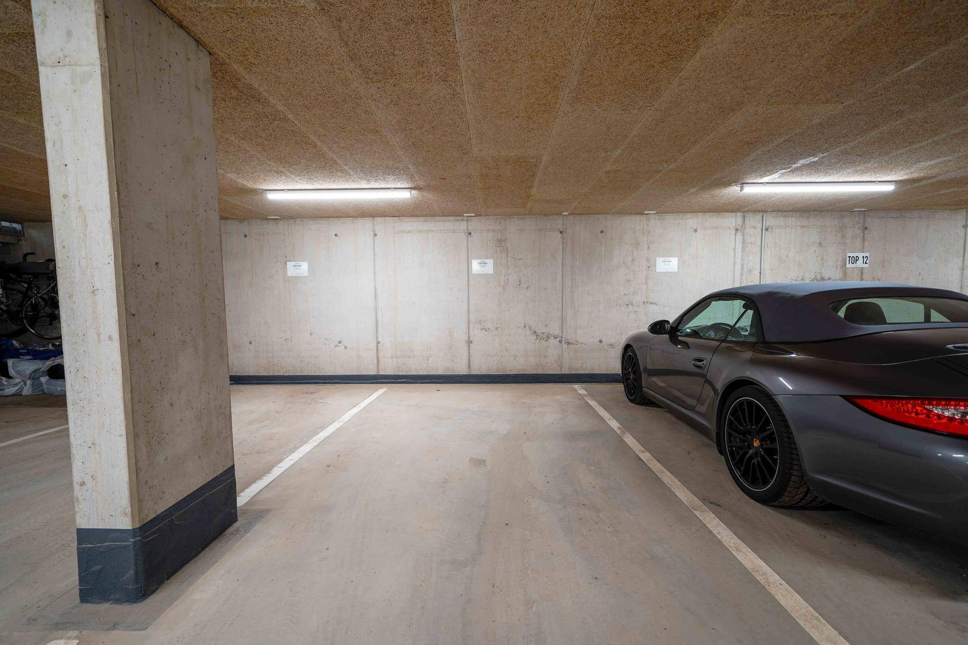 Geräumiger Tiefgaragenstellplatz mit Betonwänden und einer Decke aus Holzfaserplatten, beleuchtet von LED-Leuchten.