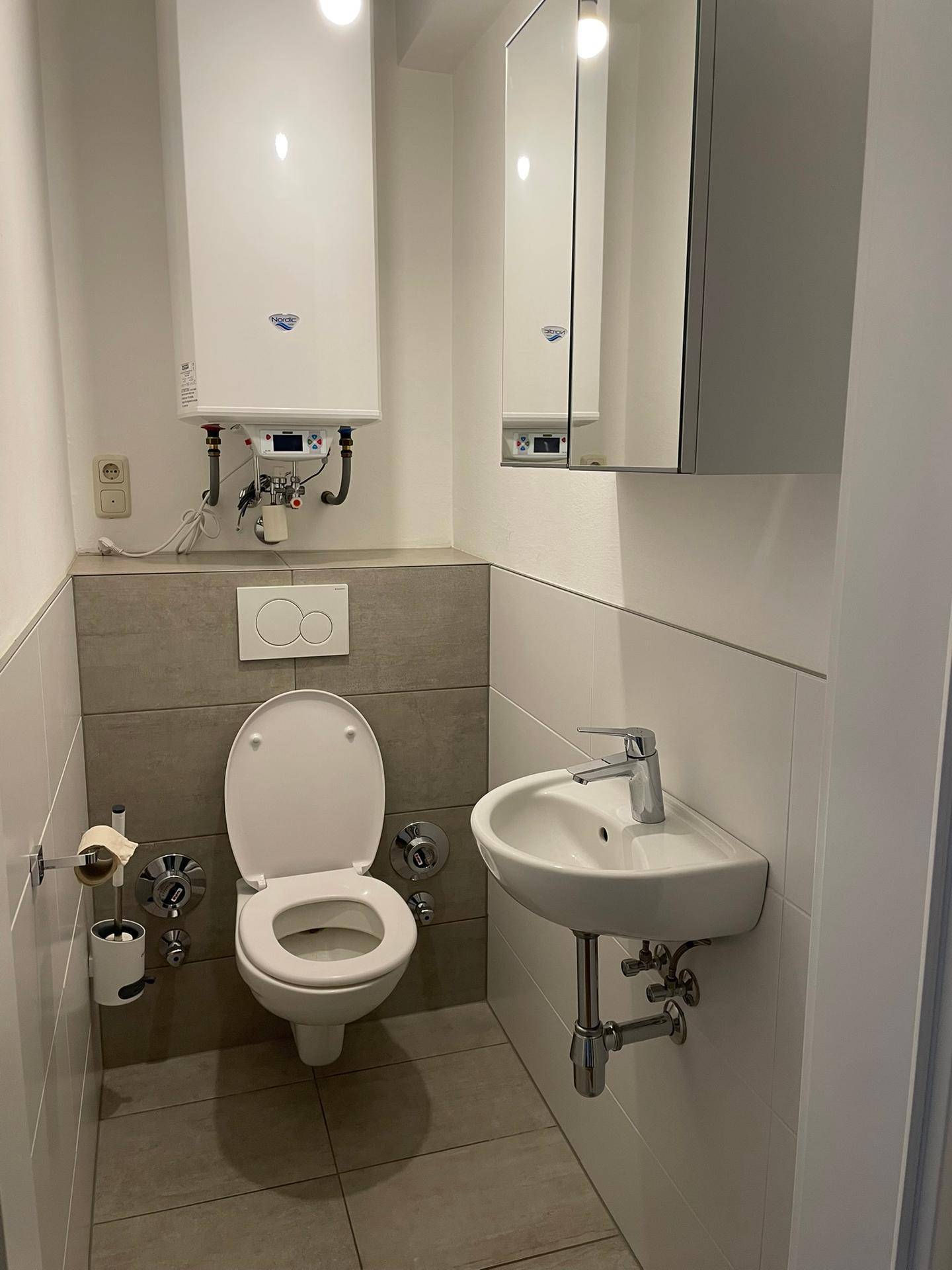Kleines Gäste-WC mit Toilette, Waschbecken und Spiegelschrank.