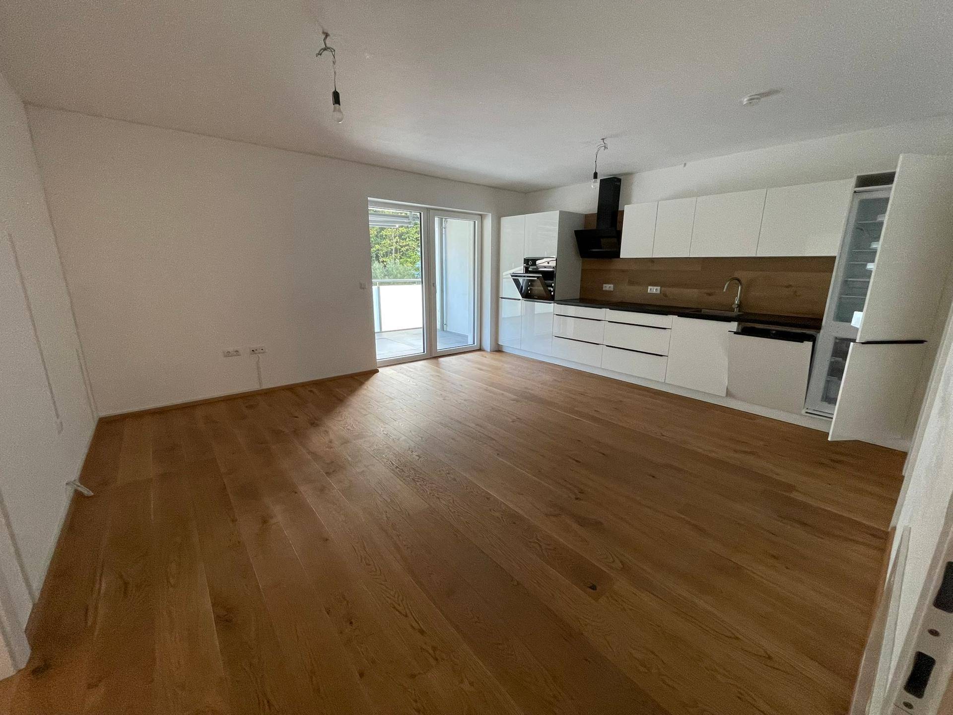 Geräumiger, unmöblierter Wohn-Essbereich mit moderner Einbauküche und Zugang zum Balkon.
