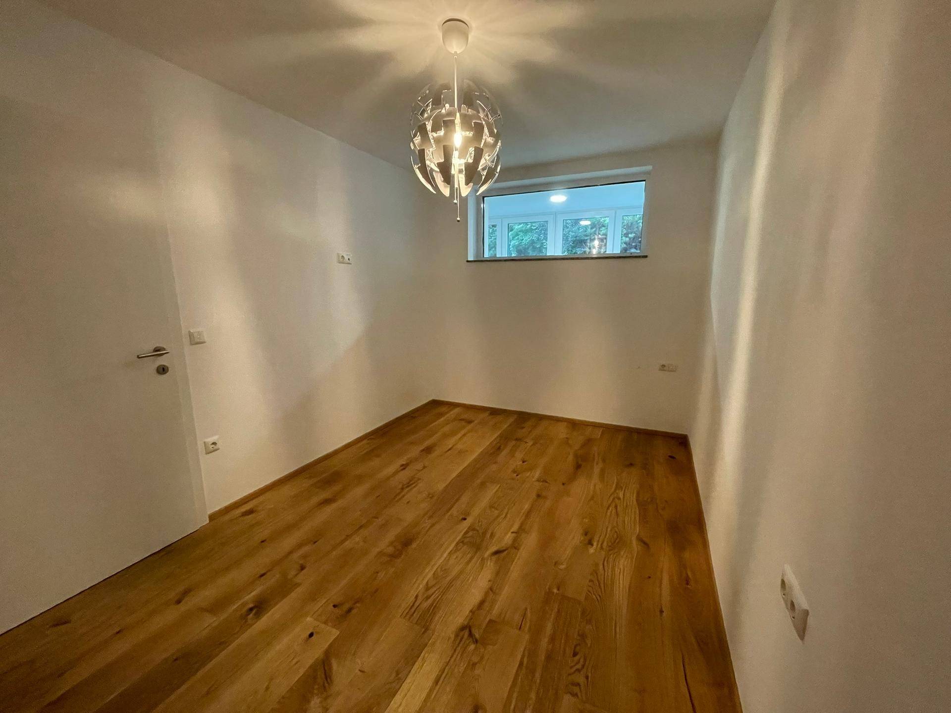 Helles, unmöbliertes Schlafzimmer mit Holzboden und einem Fenster.