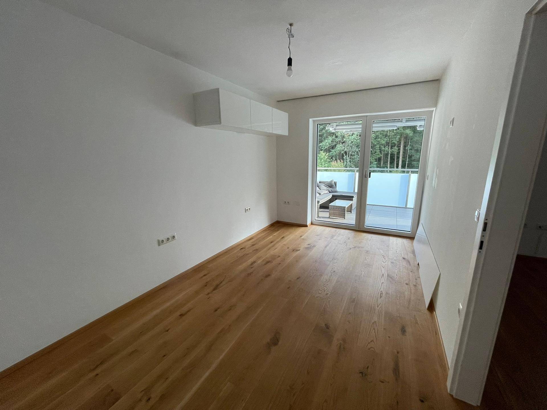 Geräumiges, unmöbliertes Kinderzimmer mit Holzboden und Zugang zum Balkon.