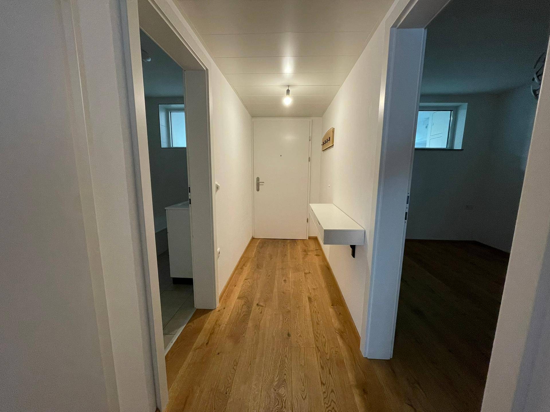 Heller Flur mit Holzboden und schlichter Einrichtung, der zu weiteren Räumen führt.