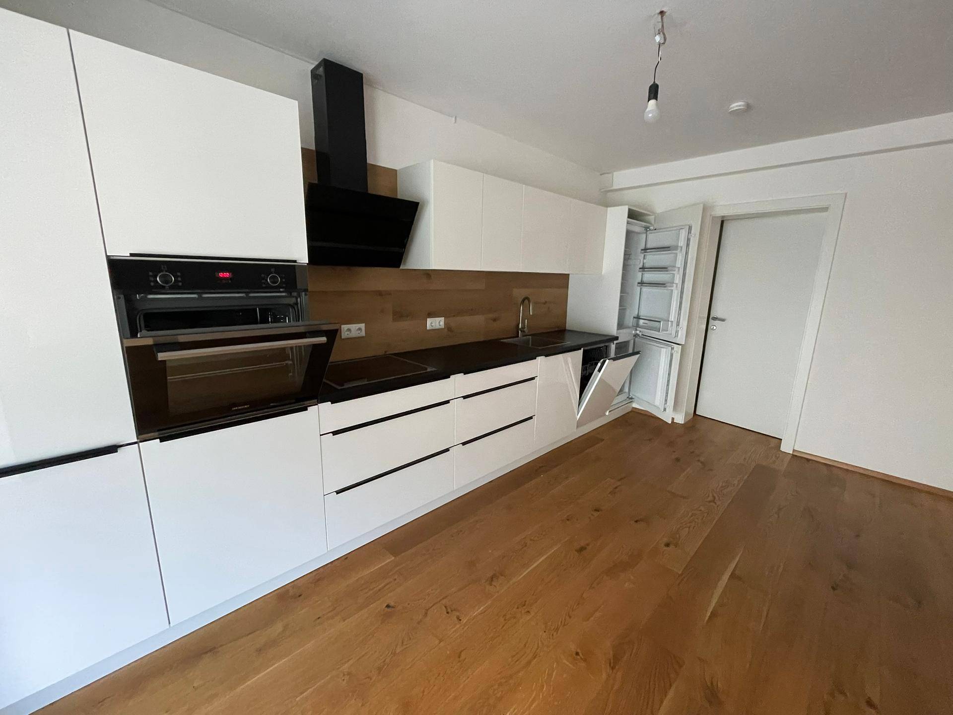 Detailansicht der modernen Einbauküche mit weißen Fronten, Holzrückwand und integrierten Geräten.