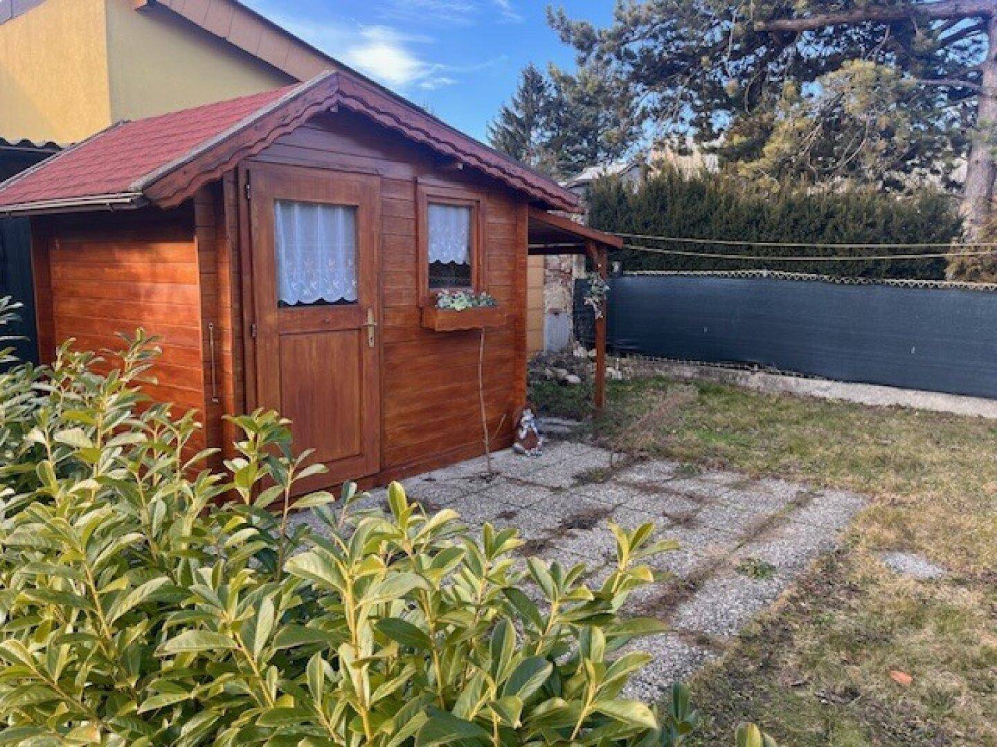 Charmantes Gartenhaus aus Holz mit Fenstern und kleiner Veranda im Grünen.