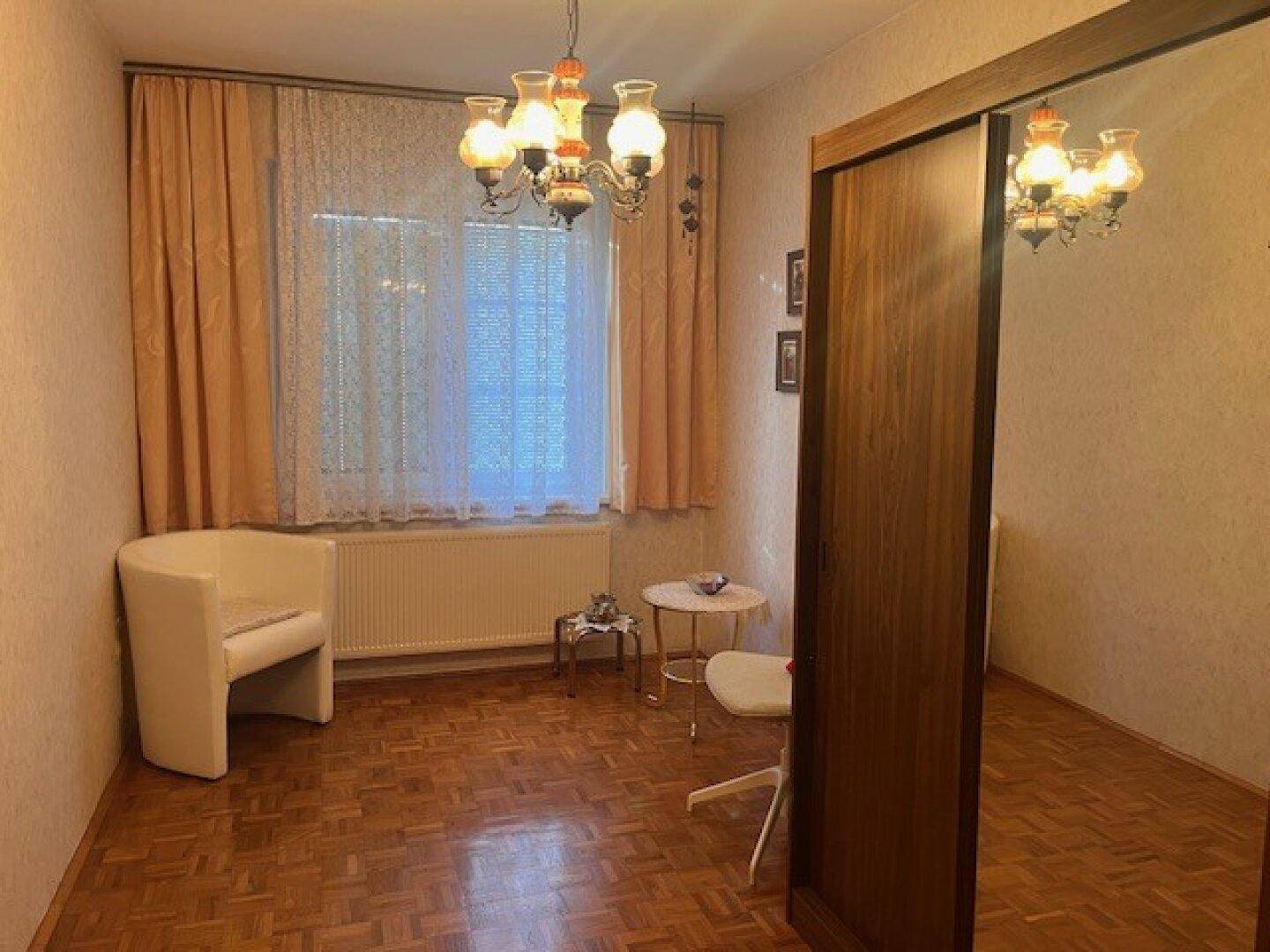 Kleines Zimmer mit Parkettboden, Fenster und traditioneller Beleuchtung, ideal als Büro oder Gästezimmer.