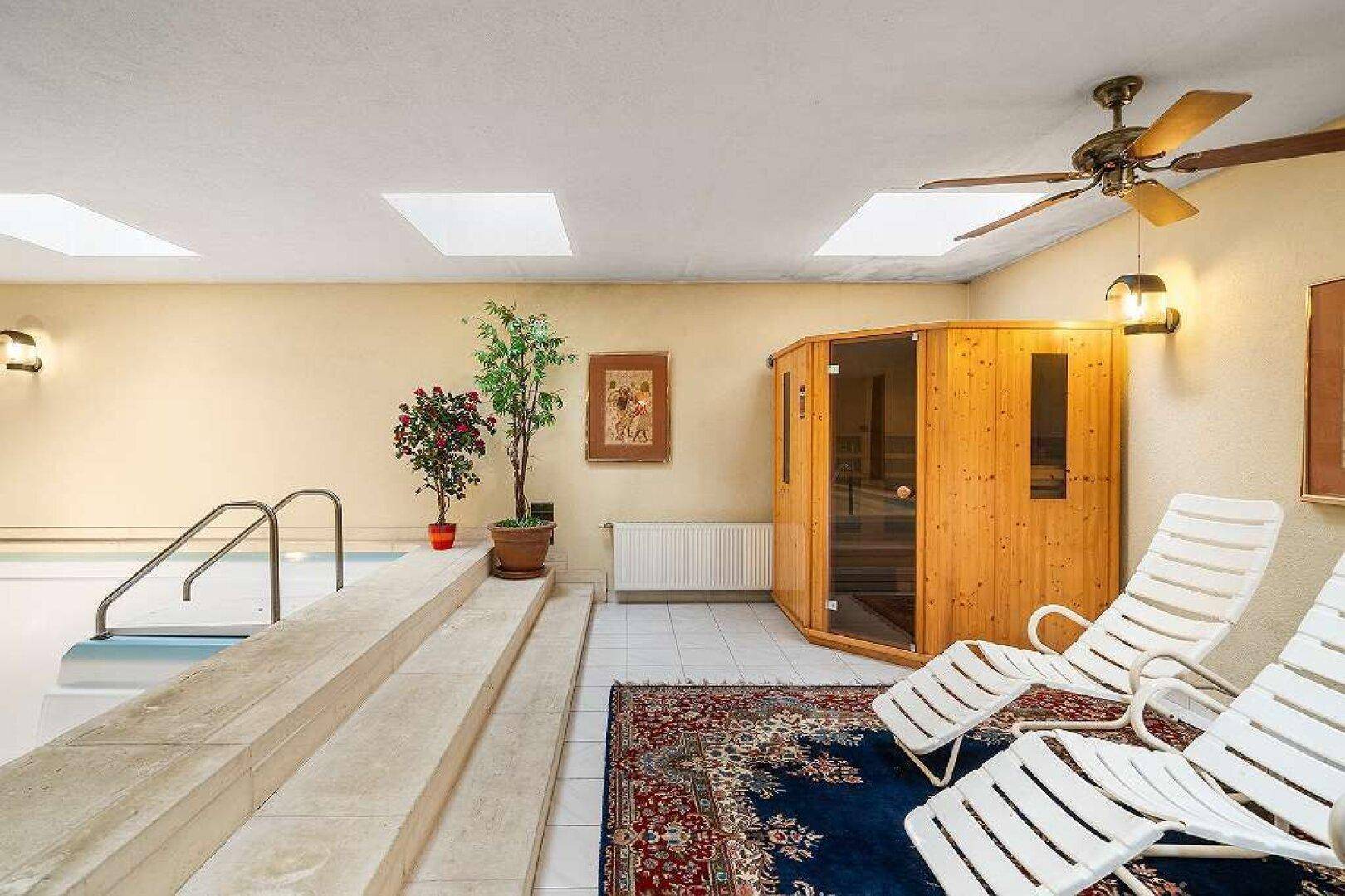 Wellnessbereich mit Innenpool, Sauna, Liegestühlen und einem Deckenventilator für Entspannung.
