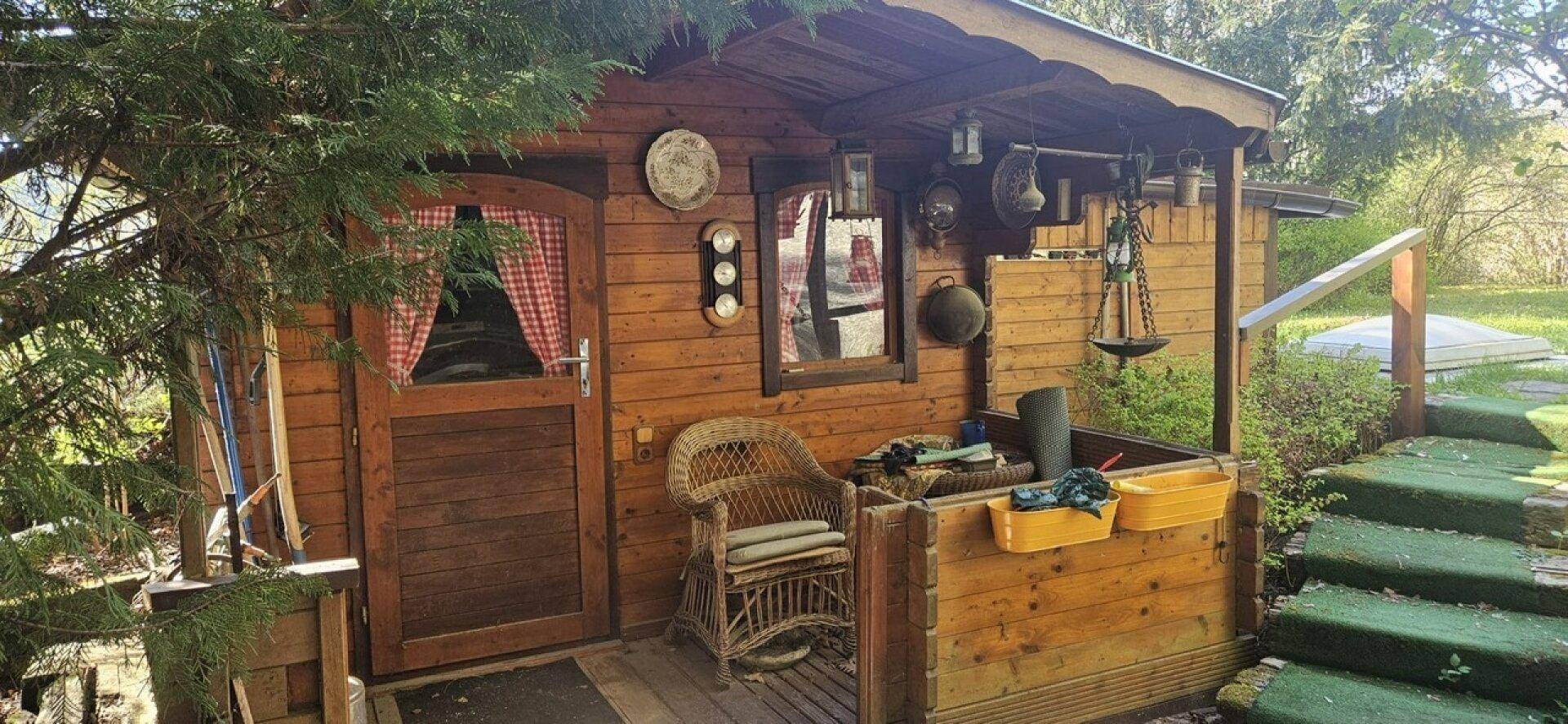 Rustikales Gartenhaus aus Holz mit kleiner Veranda und dekorativen Elementen im Grünen.