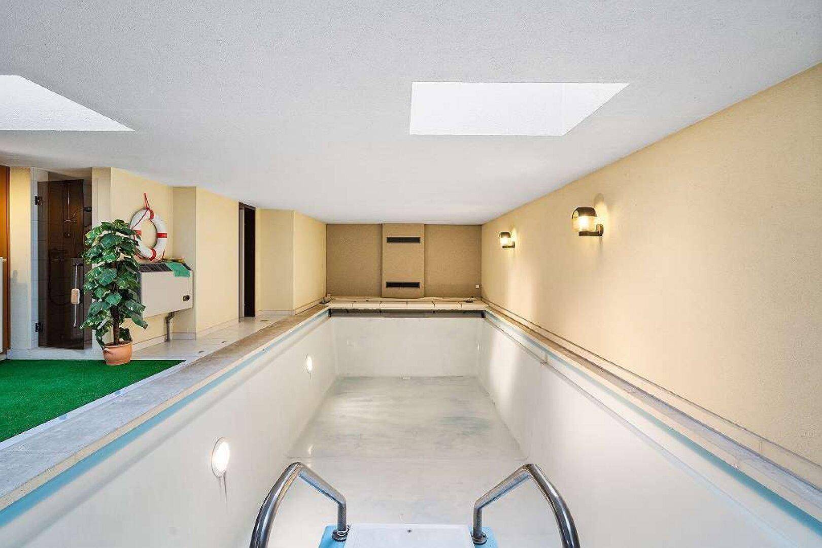 Leeres Hallenbad mit hellen Wänden, Oberlichtern und Treppen für den Zugang zum Becken.