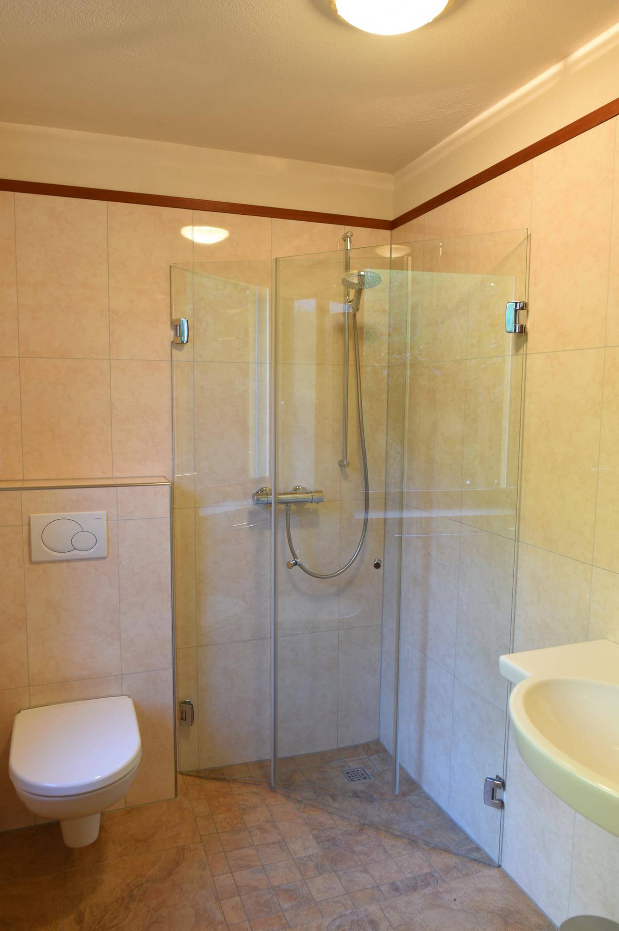 Badezimmer mit Duschkabine, wandhängendem WC und Waschbecken, gefliest in hellen Beigetönen.