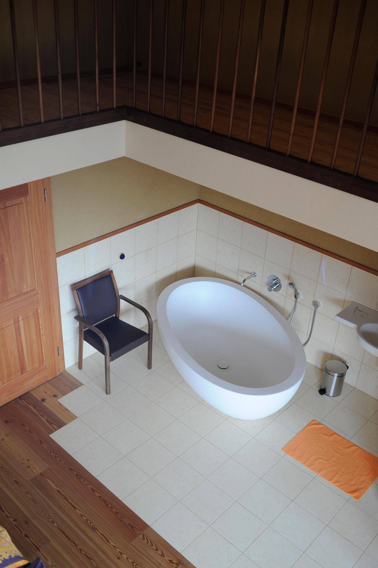 Geräumiges Badezimmer mit freistehender Badewanne und Holzboden, unter einer offenen Galerie.