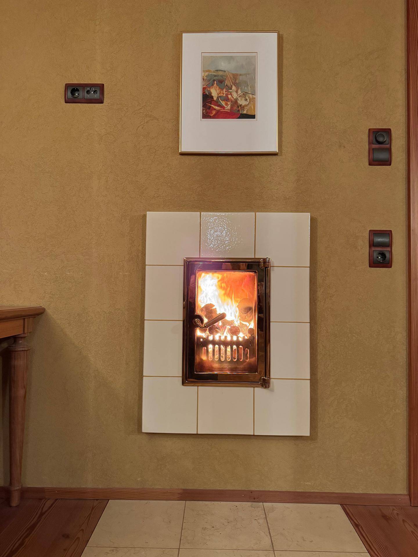 Gemütlicher Kamin mit weißer Fliesenverkleidung und warmem Feuer in einem Wohnbereich.