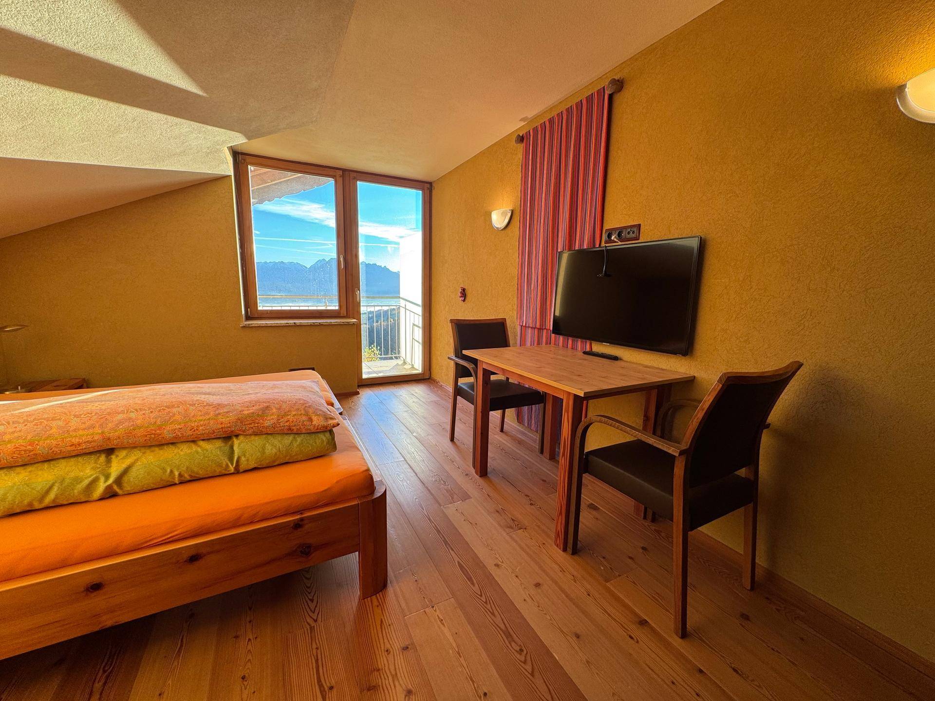 Gemütliches Schlafzimmer mit Holzboden, Bett und Tisch, bietet einen schönen Ausblick auf die Berge.