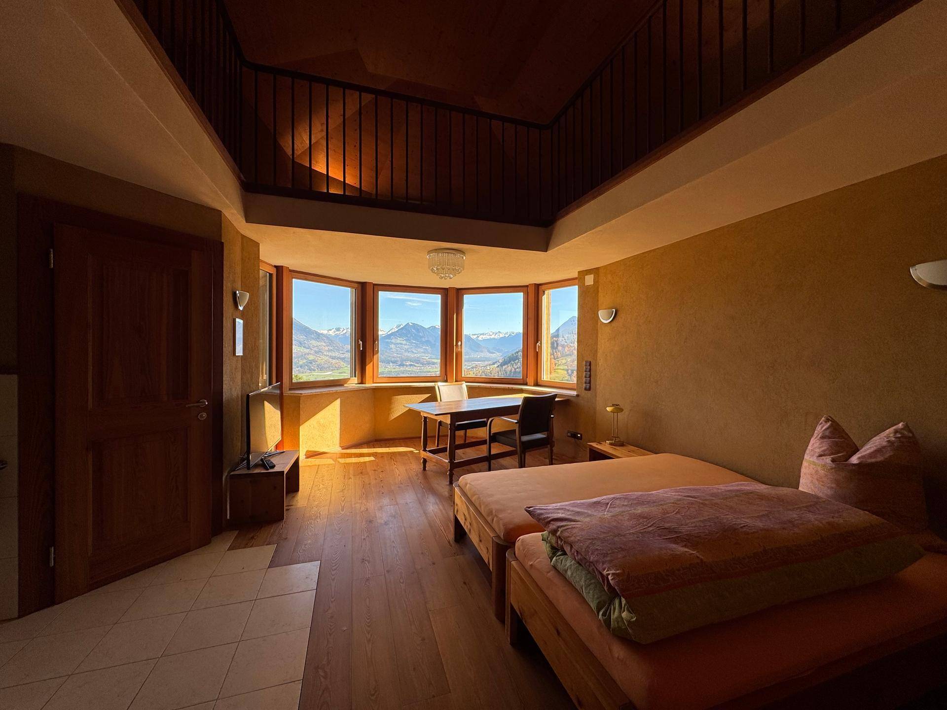 Helles Schlafzimmer mit Holzboden, zwei Betten und einem Tisch, bietet einen weiten Bergblick.