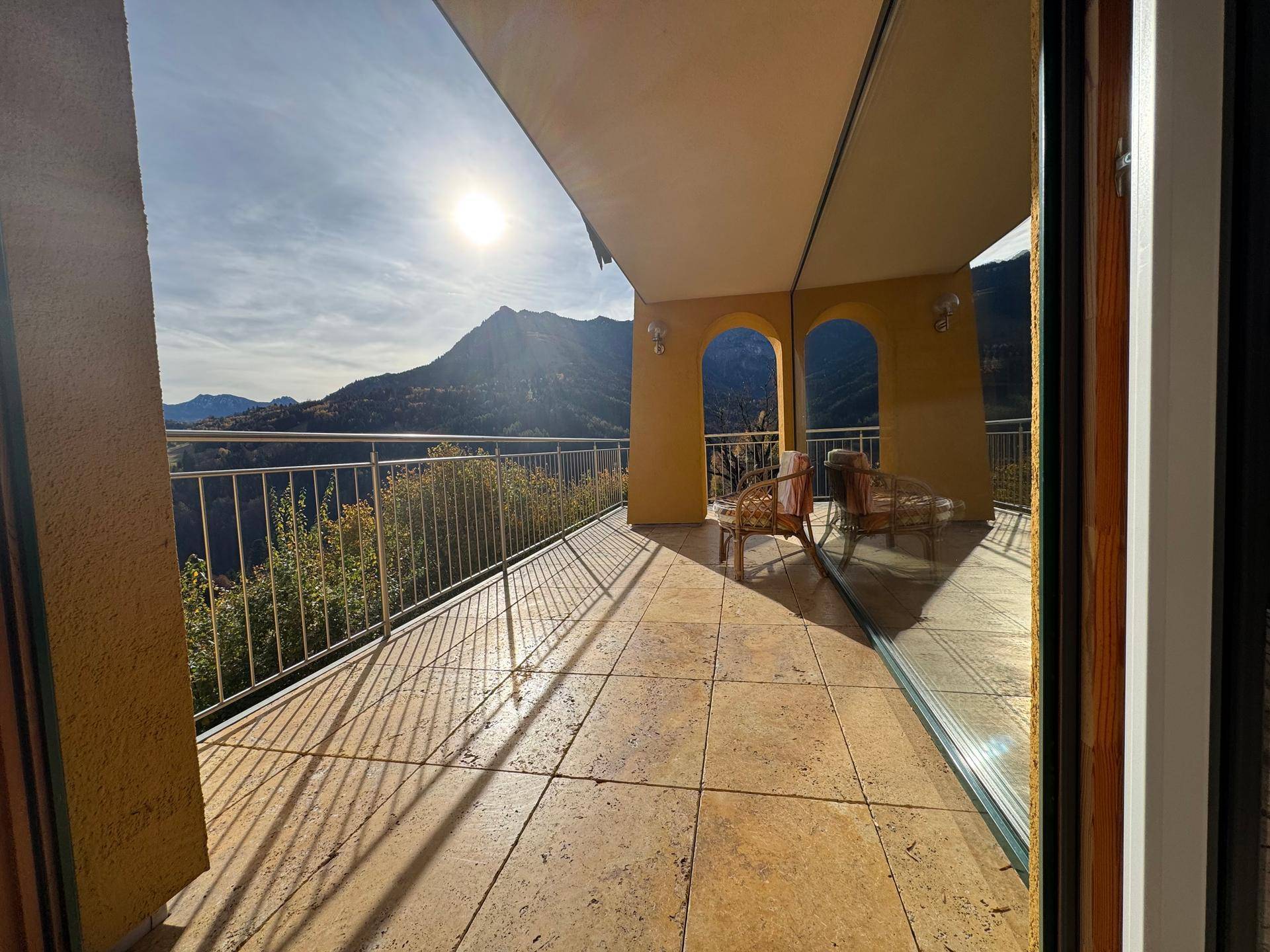 Sonnige Terrasse mit Fliesenboden und Bergblick, ausgestattet mit einem Sonnenschutz und Sitzgelegenheiten.