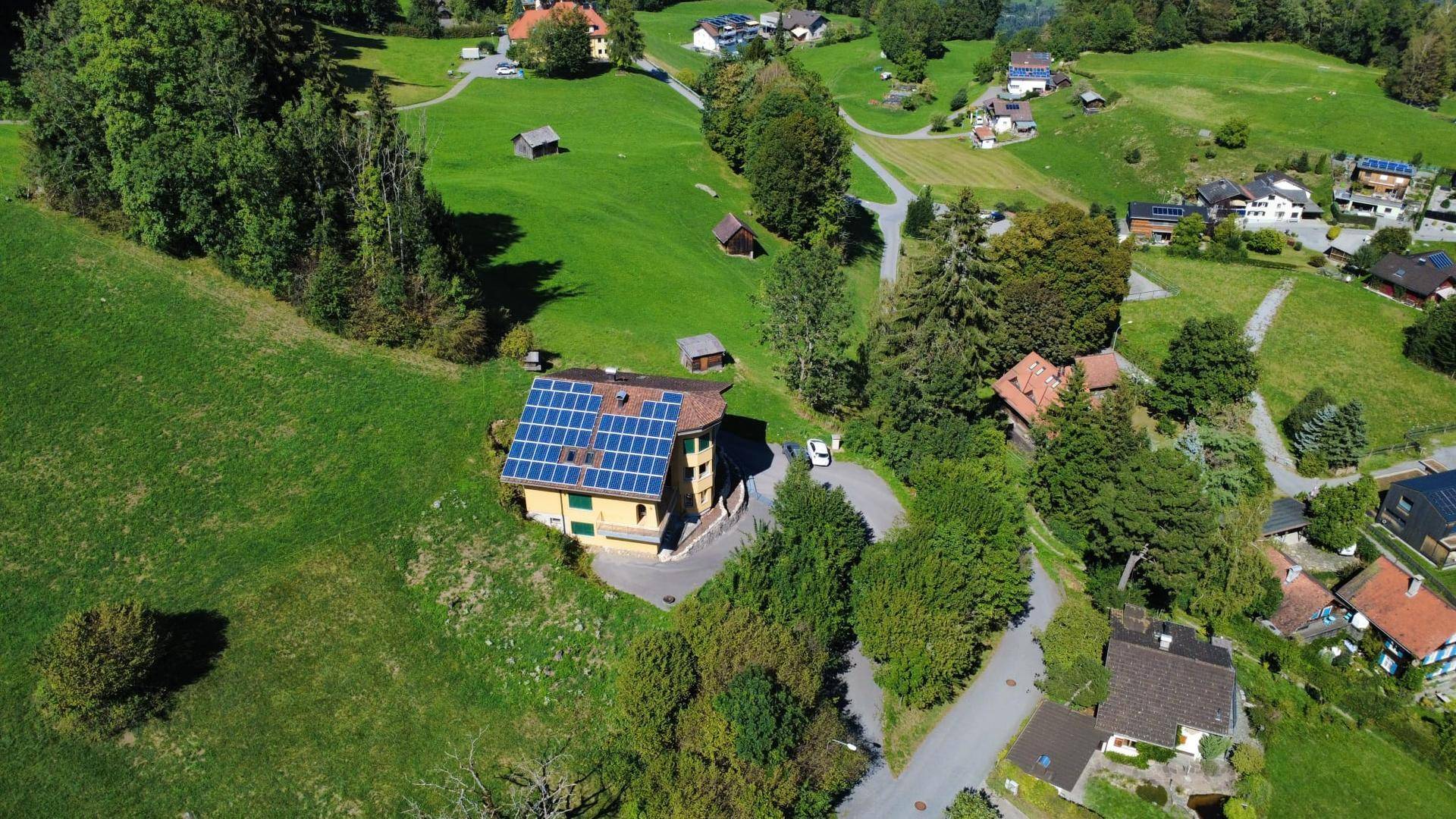 Panoramablick aus der Luft auf ein Wohnhaus mit Solarmodulen und die umliegende ländliche Siedlung.