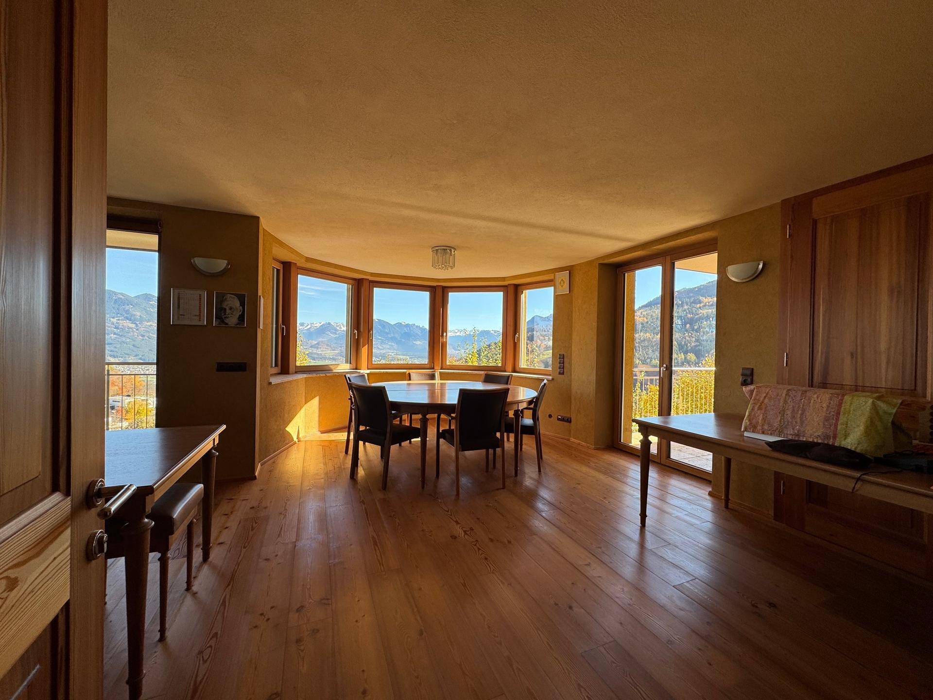 Heller Essbereich mit Holzboden, großen Fenstern und Bergblick, ideal für gesellige Runden.
