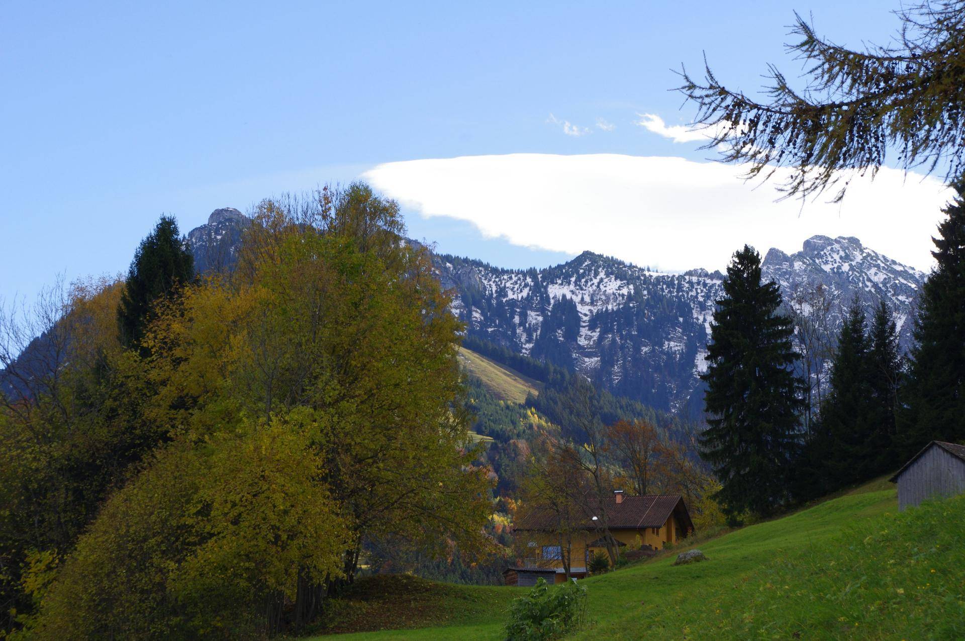 Malerische Berglandschaft mit herbstlichen Bäumen und einem kleinen Haus im Tal unter bewölktem Himmel.