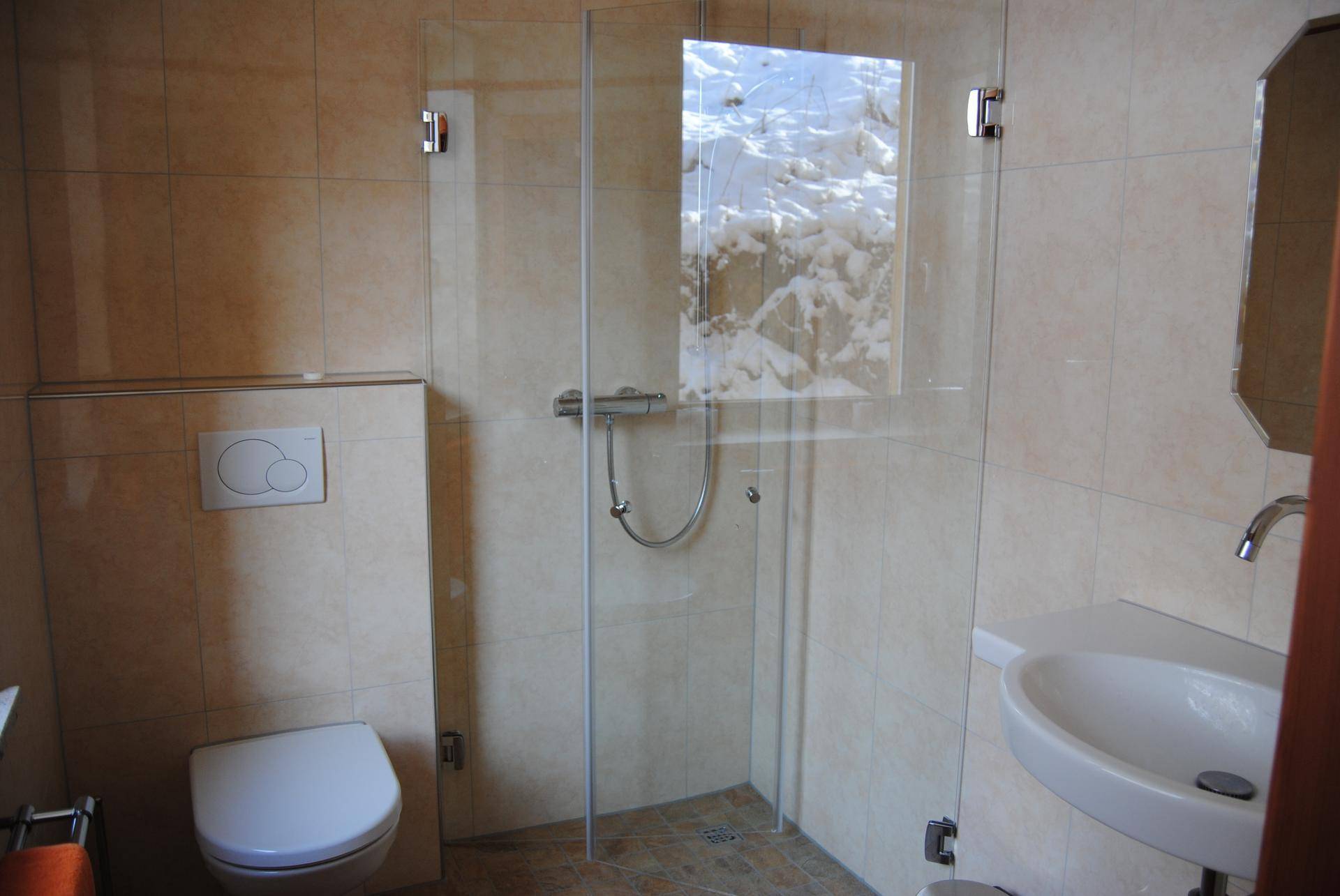 Modernes Badezimmer mit beigefarbenen Fliesen, wandhängendem WC und einer Glasdusche.