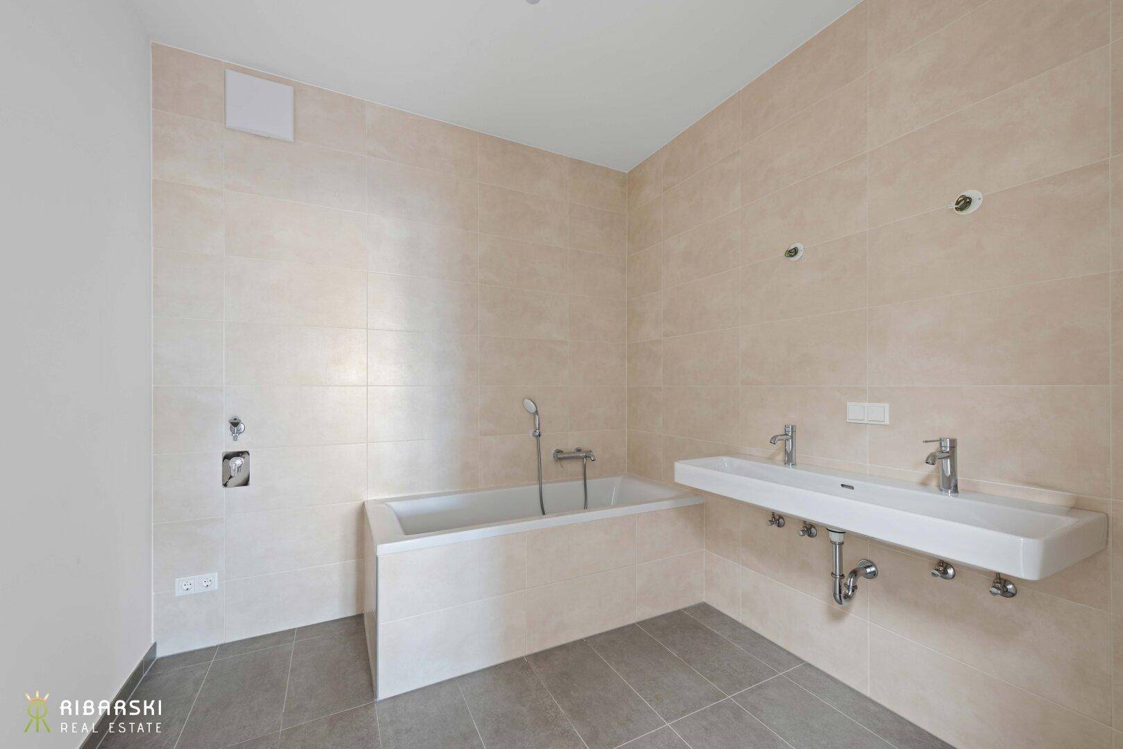 Modernes Badezimmer mit beigefarbenen Wandfliesen, integrierter Badewanne und Doppelwaschbecken.