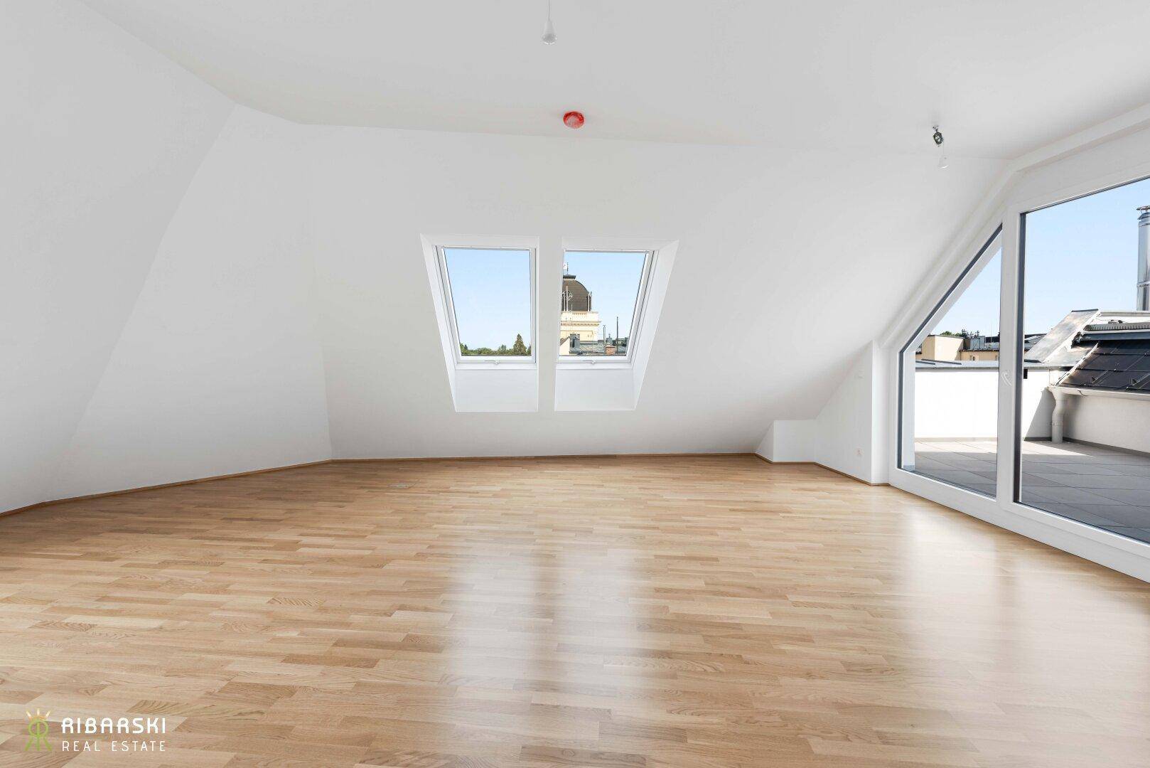 Heller Dachgeschossraum mit Holzboden, Dachfenstern und Zugang zu einer Terrasse.