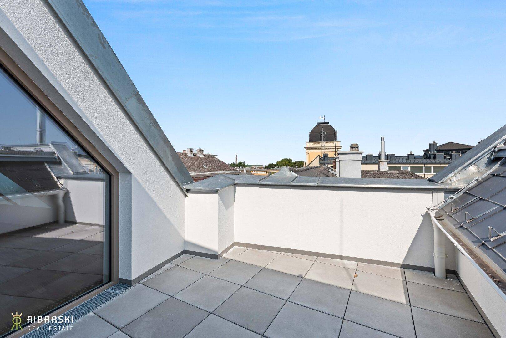 Geräumige Dachterrasse mit Fliesenboden und weitem Blick über die umliegenden Dächer der Stadt.