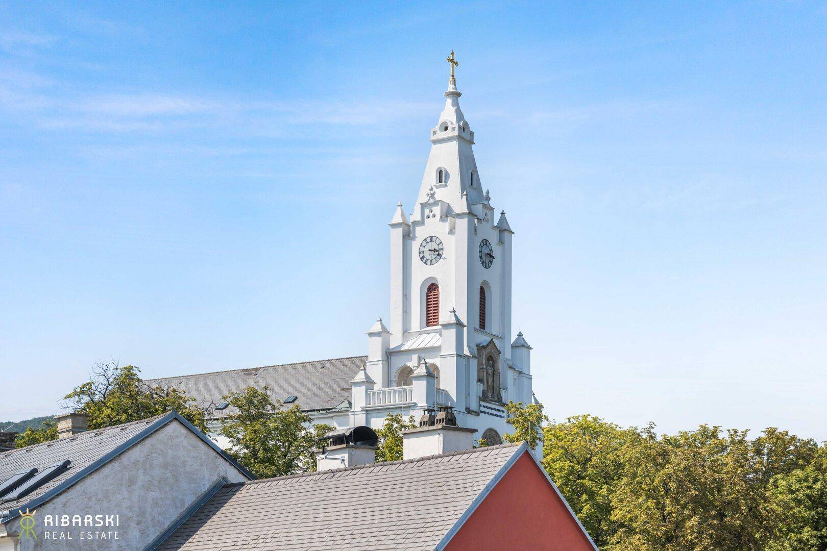 Blick auf eine historische Kirche mit hohem Turm und Uhrwerk über den Dächern.