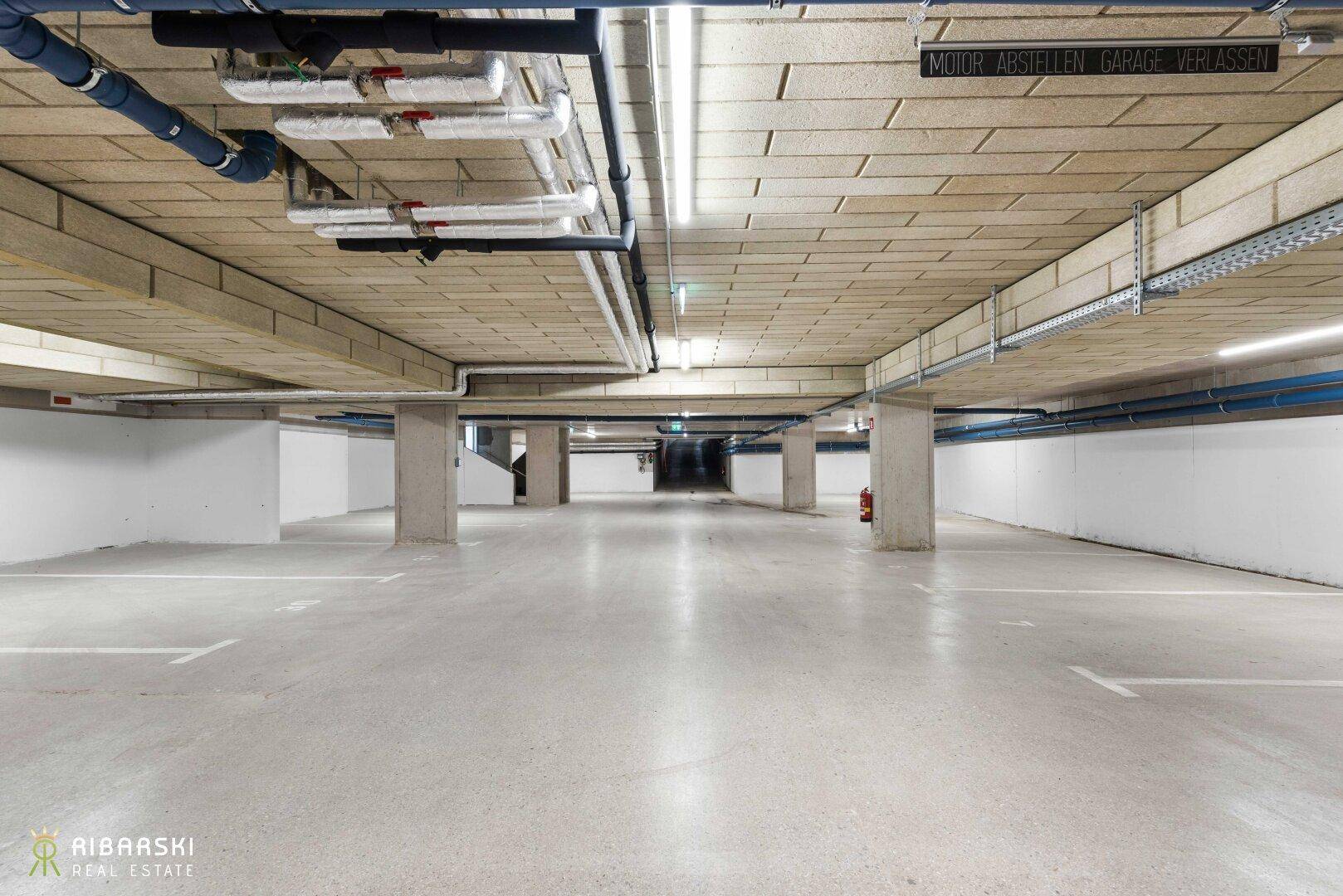 Geräumige Tiefgarage mit Betonboden und sichtbaren Installationen an der Decke.