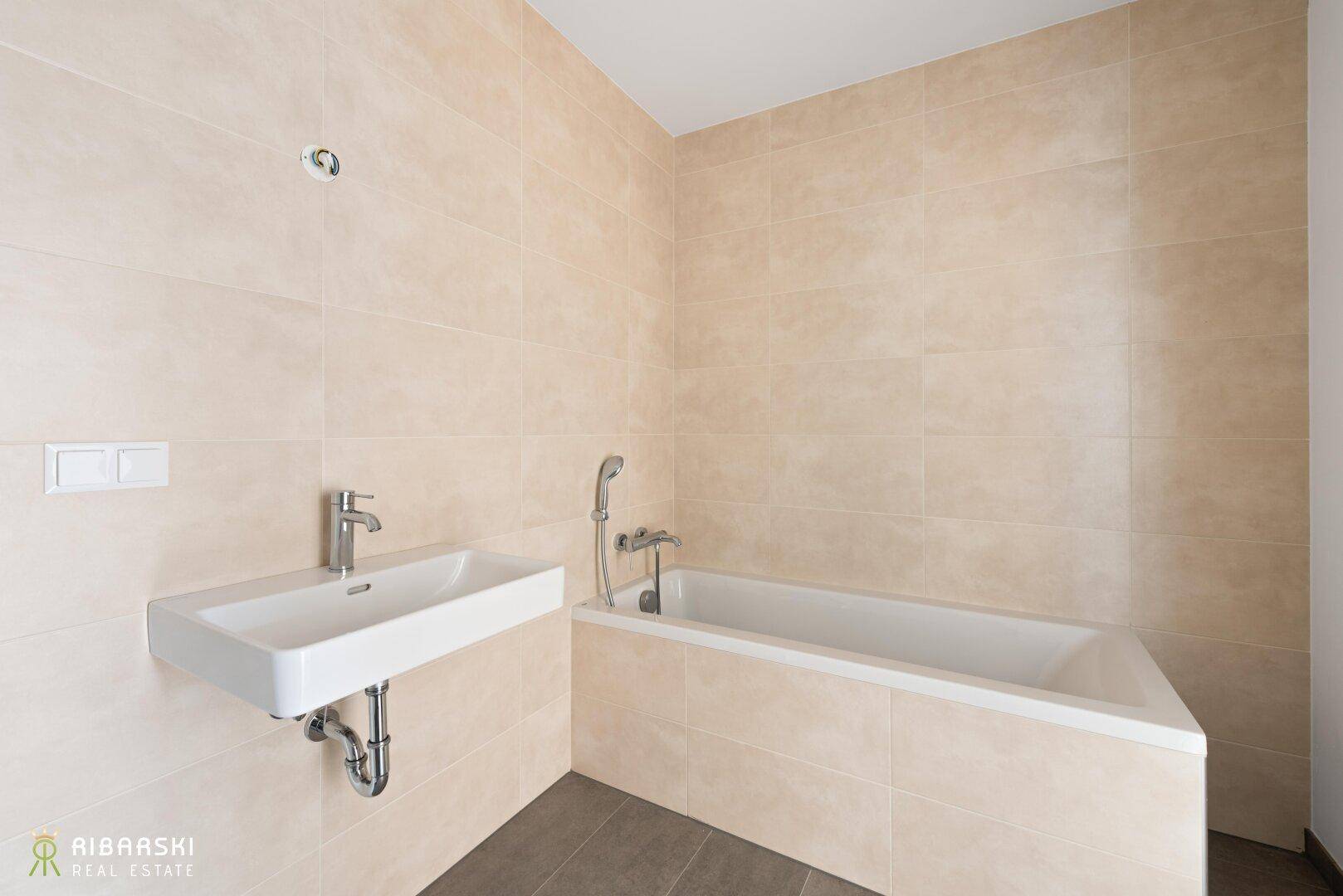 Modernes Badezimmer mit beigefarbenen Fliesen, Waschbecken und einer Badewanne.