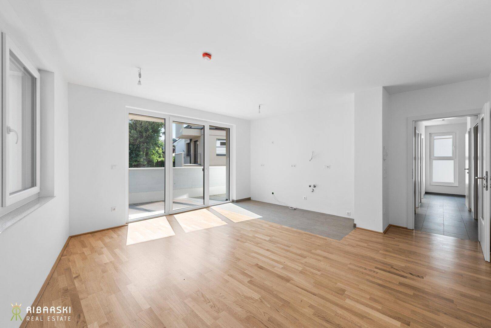 Geräumiges Wohnzimmer mit Parkettboden und großen Schiebetüren zum Balkon.