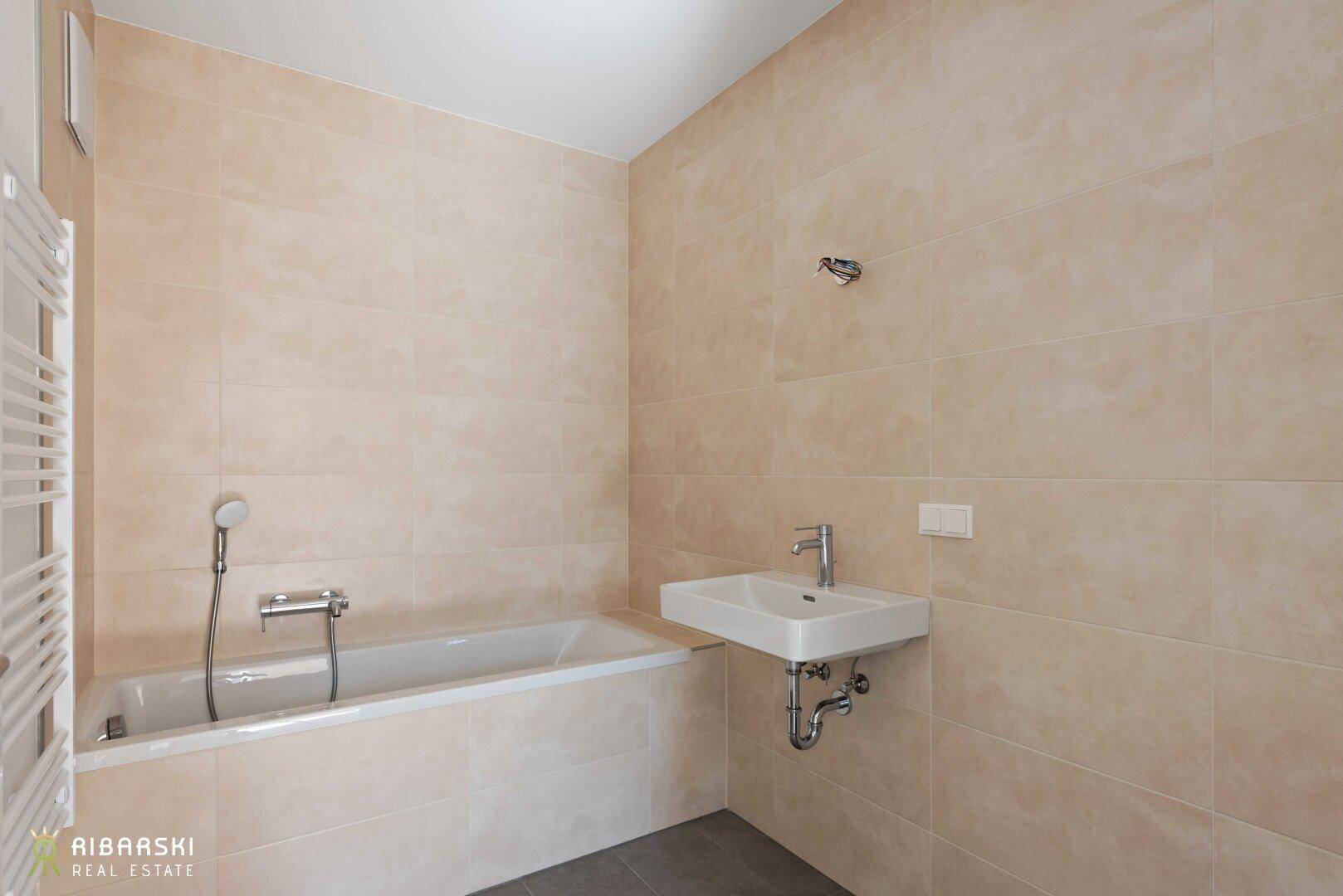 Modernes Badezimmer mit Badewanne, Einzelwaschbecken und beigefarbenen Fliesen, inklusive Handtuchheizkörper.