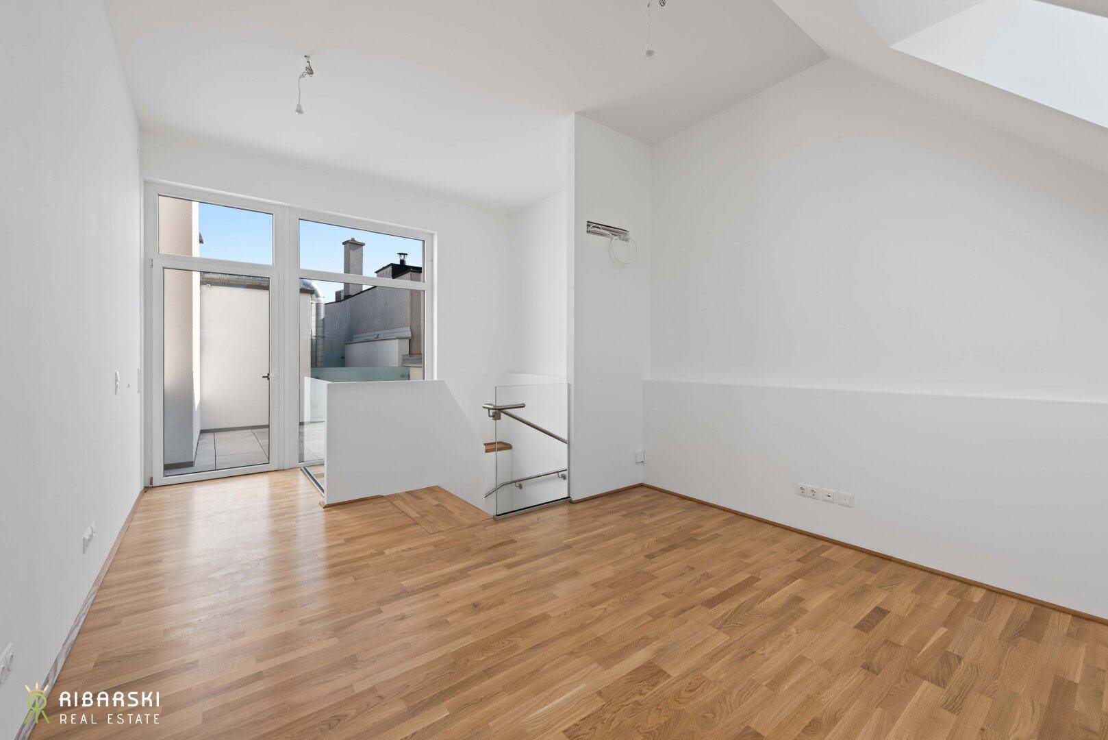 Heller Wohnbereich mit Parkettboden, Zugang zur Terrasse und moderner Treppe mit Glasgeländer.