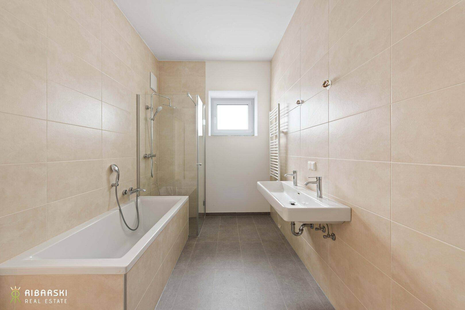 Modernes Badezimmer mit beigefarbenen Fliesen, Badewanne, Dusche und Doppelwaschbecken.