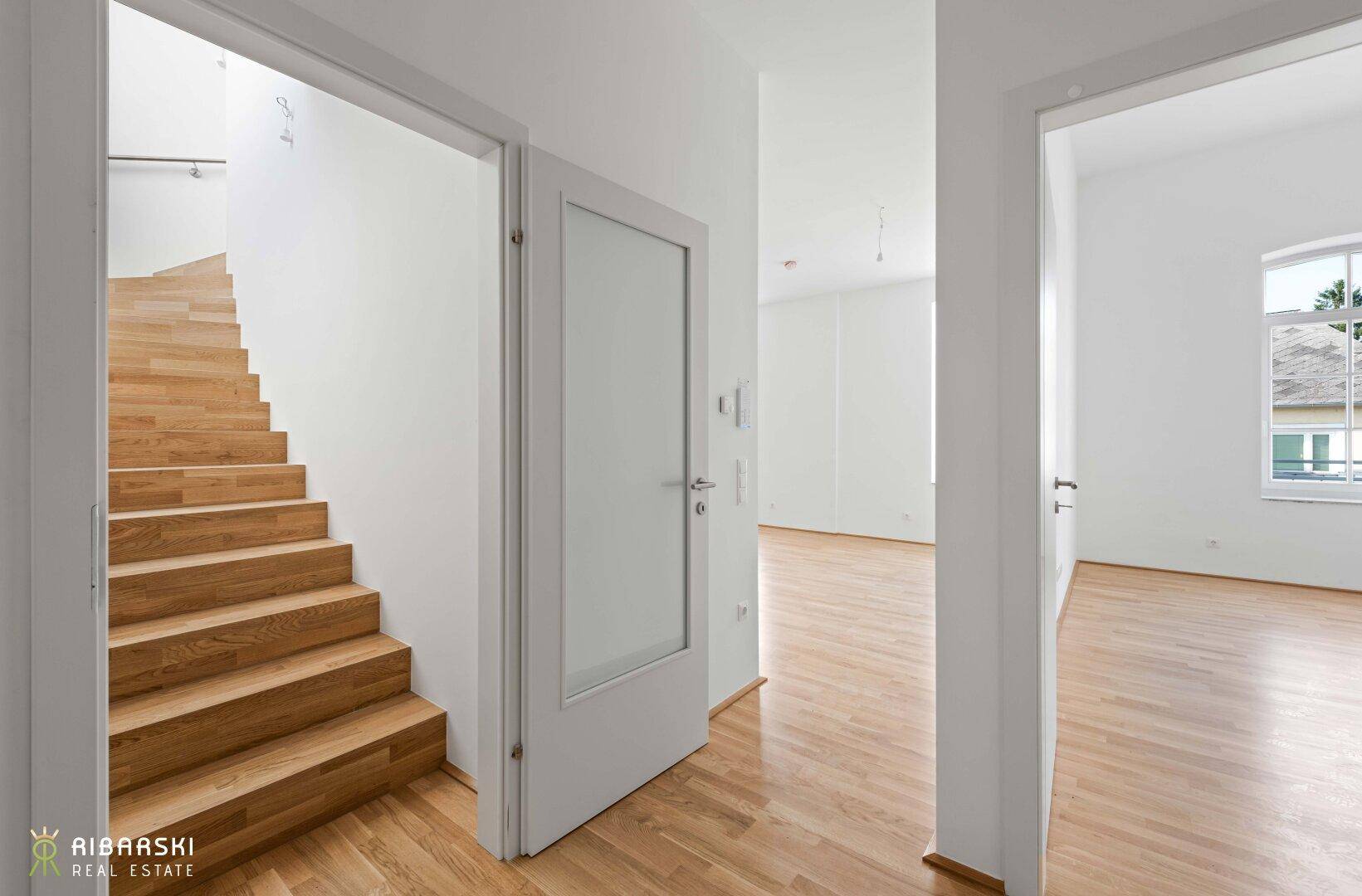 Heller Flur mit Holztreppe und Parkettboden, der zu weiteren Räumen führt.