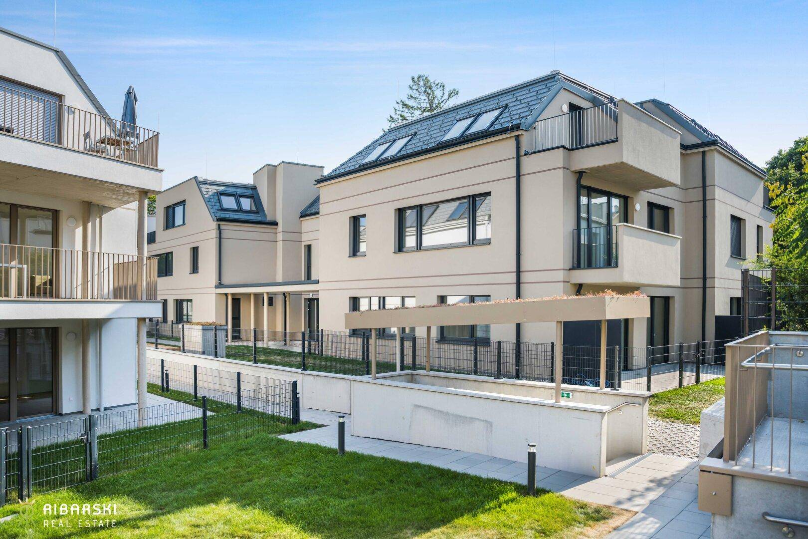 Modernes Mehrfamilienhaus mit hellen Fassaden, Balkonen und gepflegten Grünflächen in sonniger Lage.