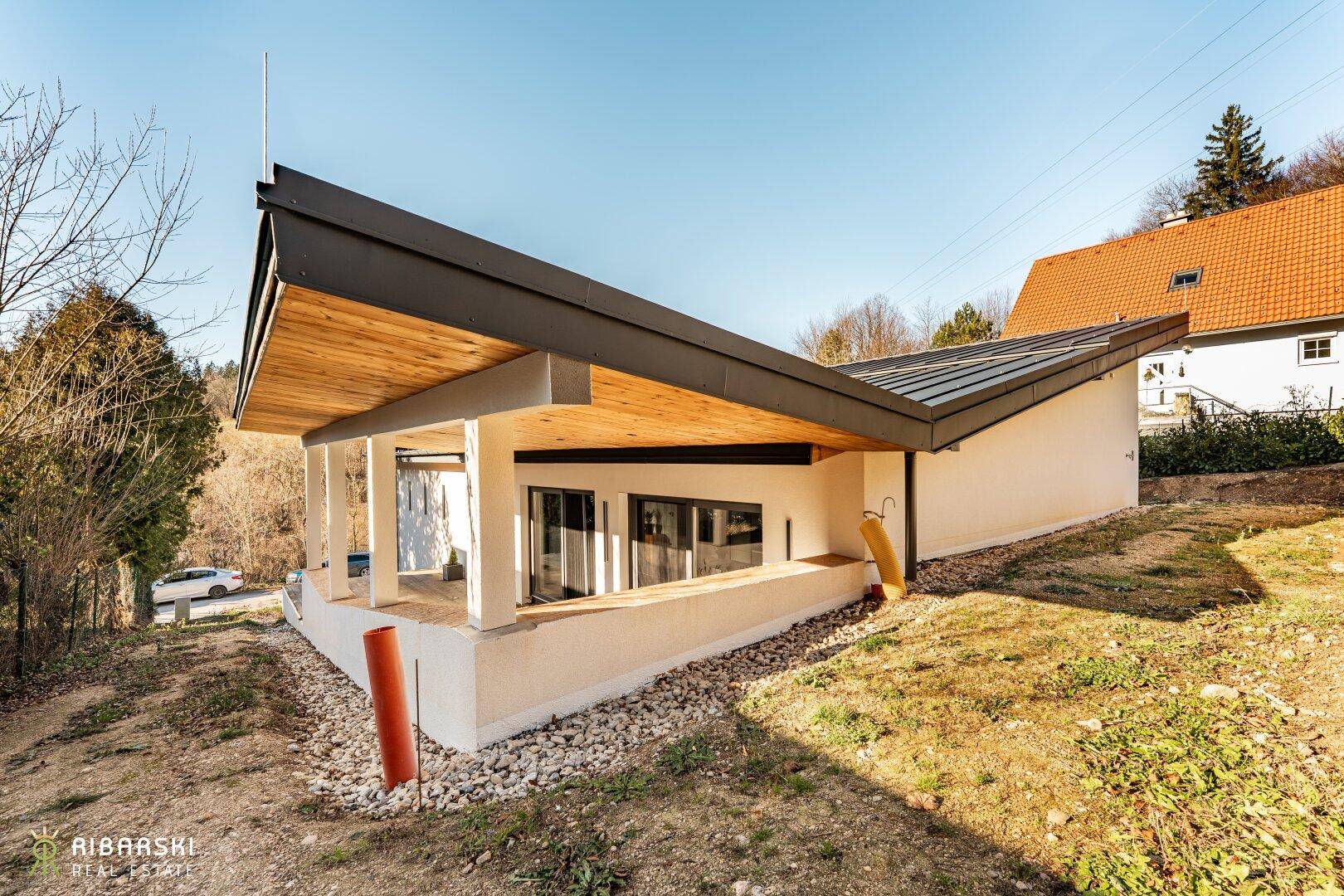Seitenansicht des modernen Hauses mit schrägem Dach, großen Fenstern und natürlicher Umgebung.