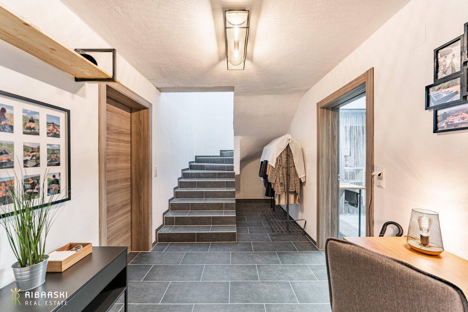 Heller Flur mit Treppe, Fliesenboden und modernem Lichtkonzept.